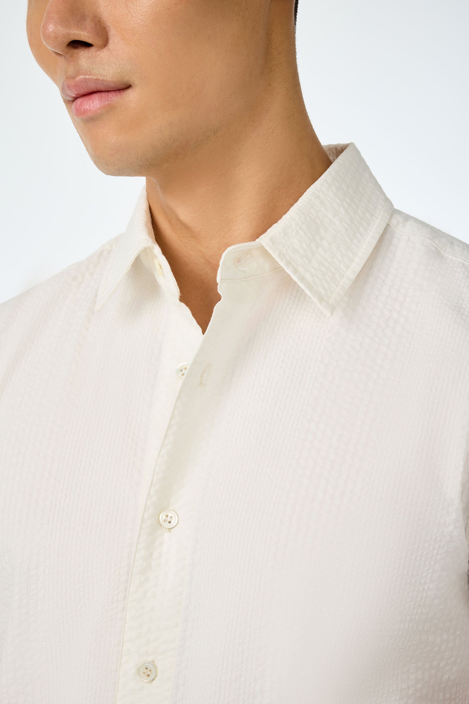 Close-up of a person wearing the Slim Jim Short-Sleeve Shirt—a textured white button-up with a pointed collar—showing their lower face, neck, and chest against a plain light background.
