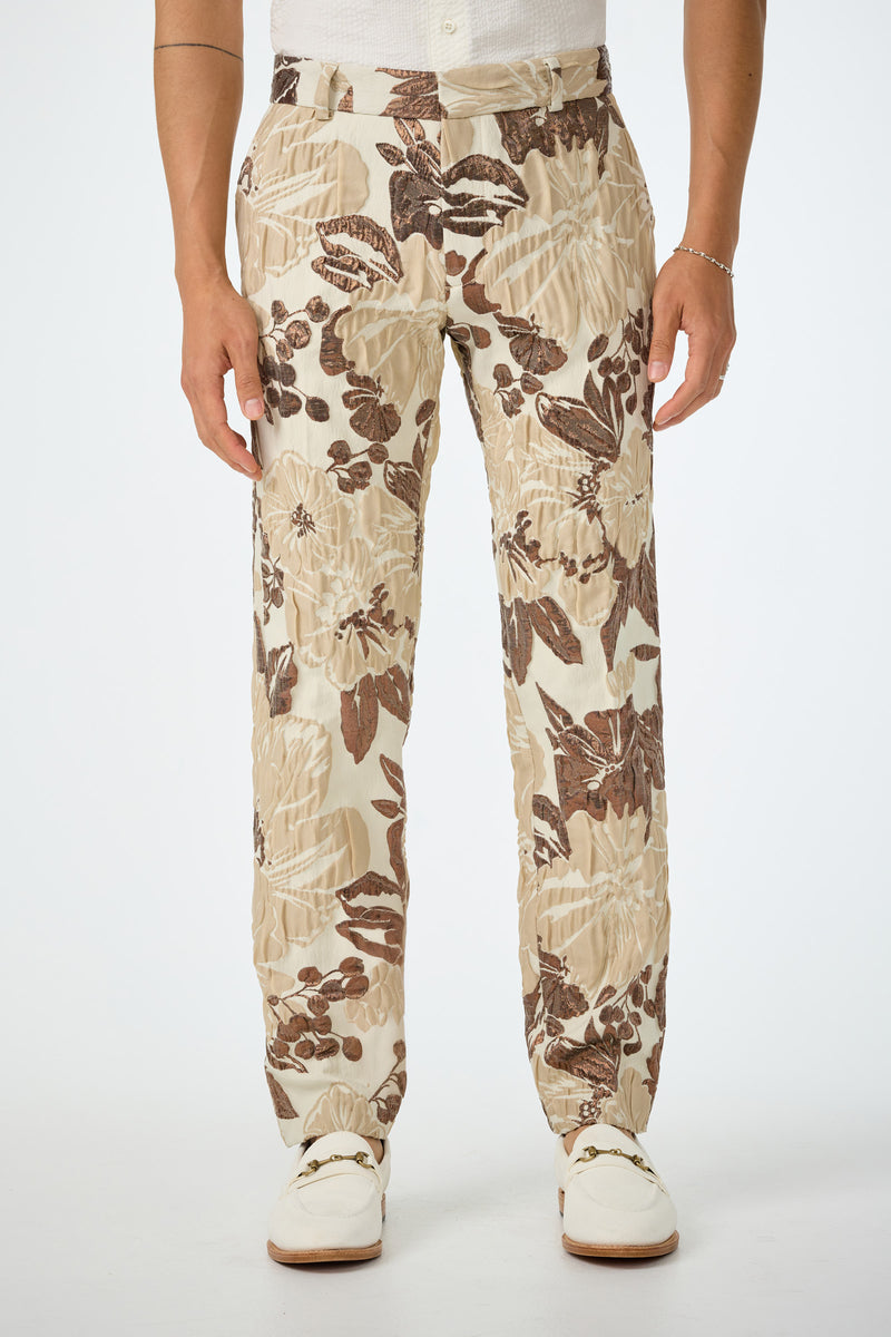 A person wearing the Clyde Slim Trouser in Daintree Jacquard, styled with a white shirt and white shoes, stands against a plain white background.