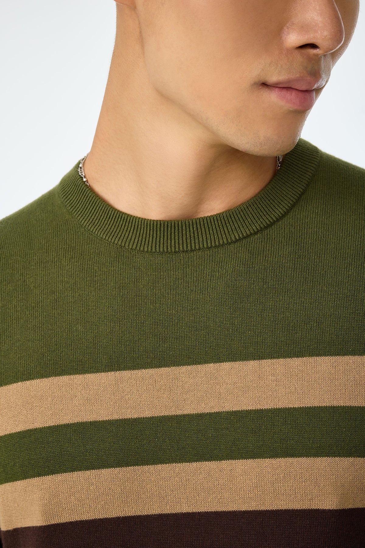 Close-up of a person wearing the Romero Crewneck Sweater in olive green with tan and dark brown stripes, showing the lower half of the face, neck, and upper chest.
