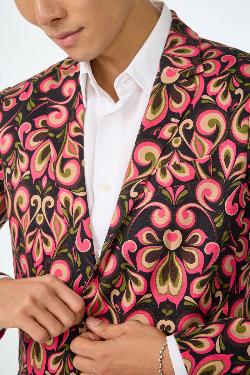 A person wearing a white dress shirt and the Thurston Blazer - Sanctuary, featuring bold pink, green, and black swirling patterns, is buttoning the jacket. Only their lower face and upper body are visible.