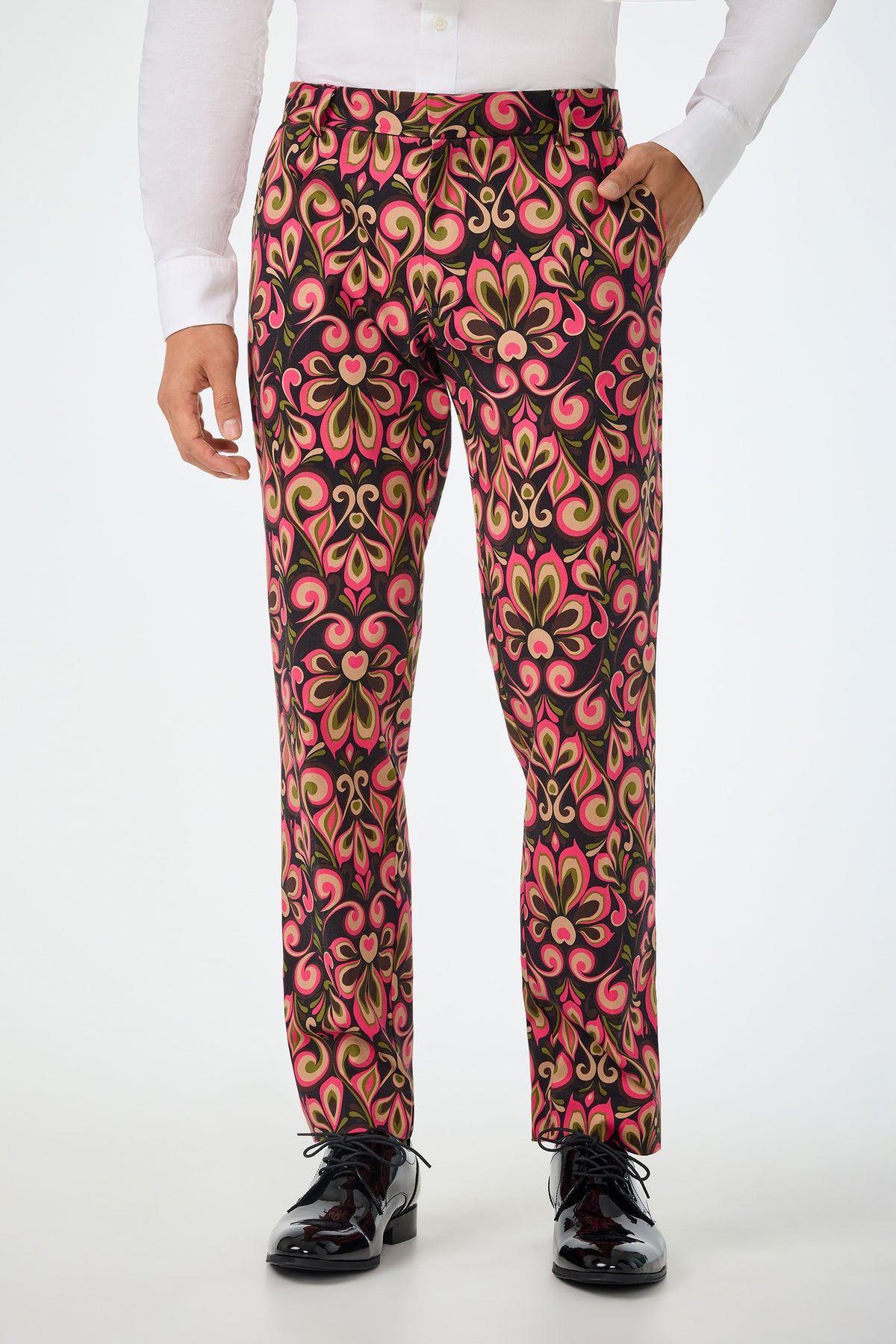 A person wearing black shoes, a white dress shirt, and the Clyde Slim Trouser in Sanctuary—a slim-fit pant featuring a bold, swirling pink, green, and gold floral pattern on a dark background. The image is cropped at the chest.