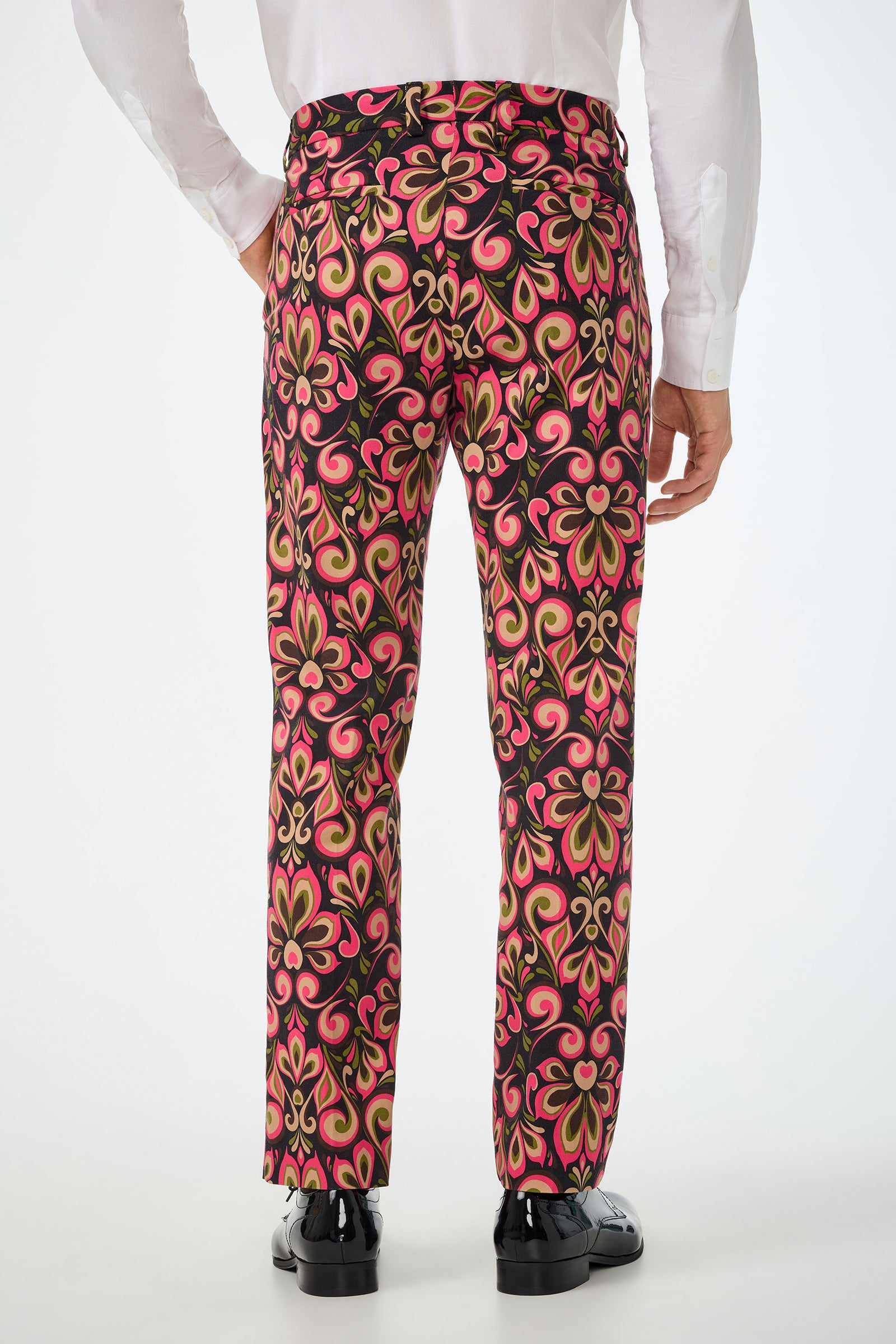 A person is seen from the back against a plain background, wearing black shoes, a white dress shirt, and the Clyde Slim Trouser - Sanctuary: colorful pants with bright pink, green, and black swirl patterns.