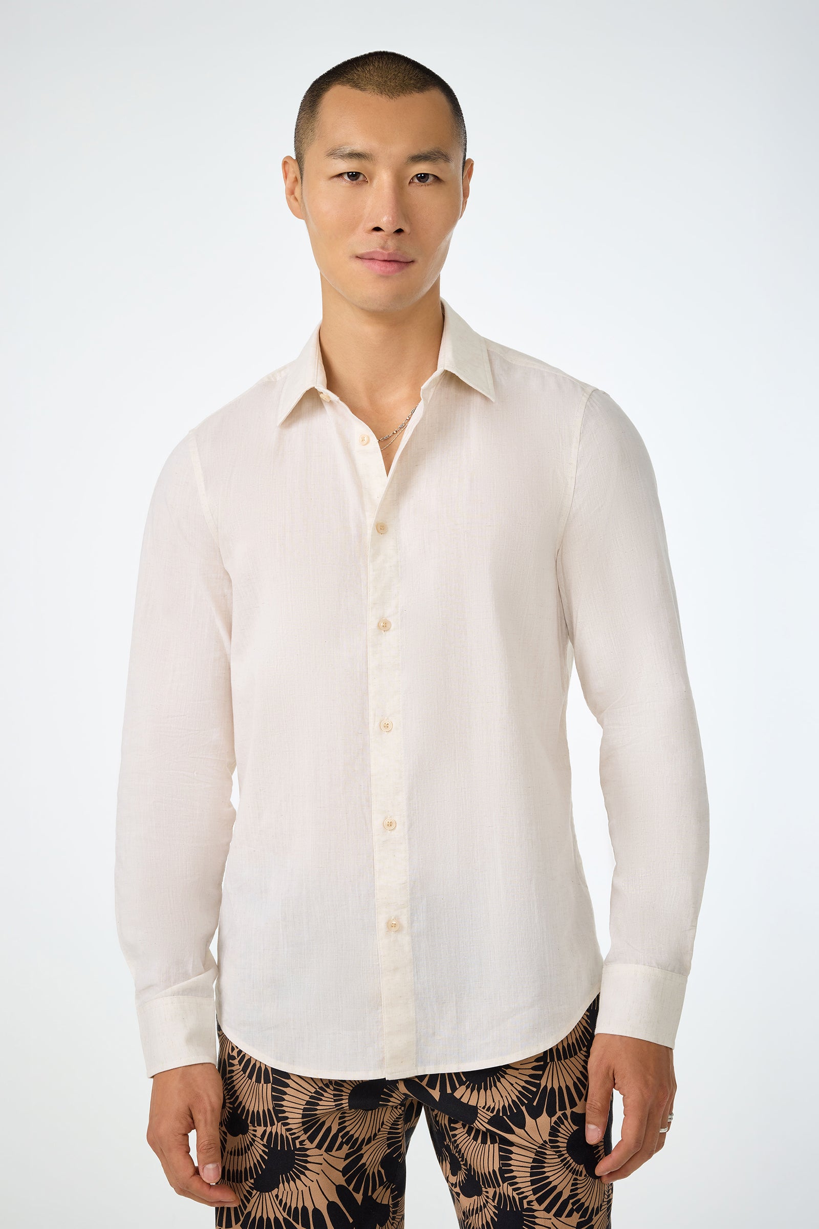 A man with short hair wears the Aaron Slim Fit Long-Sleeve Shirt in Poplar and patterned pants with a dark background and tan leaf designs, standing against a plain white background.