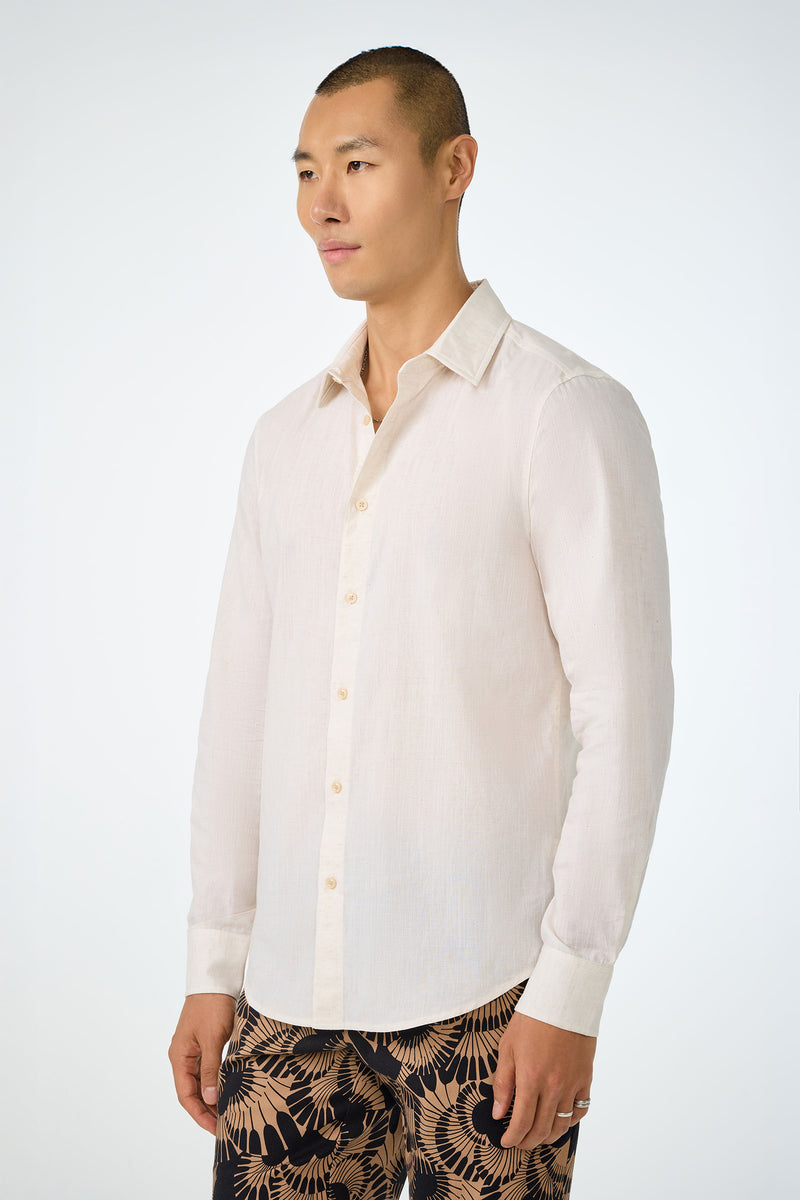 A man with short hair wears the Aaron Slim Fit Long-Sleeve Shirt in light beige and patterned black and beige pants, standing against a plain light background.