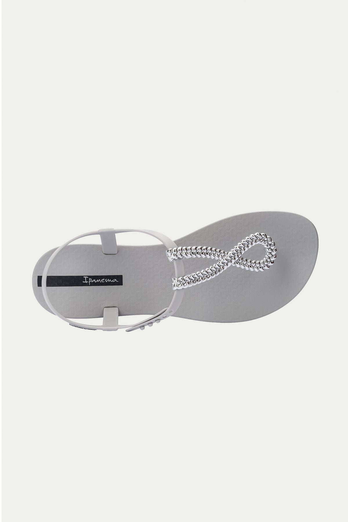 The Ipanema Class Twist Sandal - Grey is shown from above on a plain white background, featuring a light grey design with a textured sole and a silver chain strap forming a loop at the front.