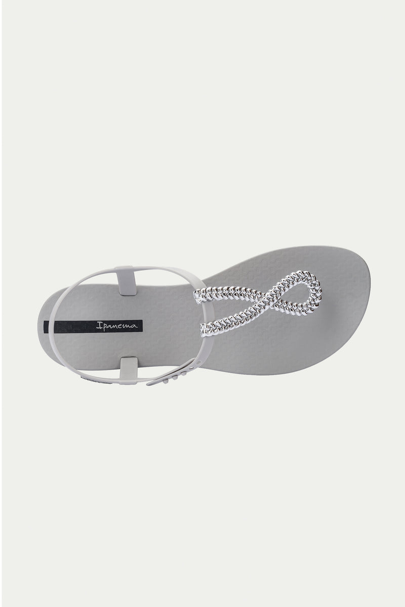 The Ipanema Class Twist Sandal - Grey is shown from above on a plain white background, featuring a light grey design with a textured sole and a silver chain strap forming a loop at the front.