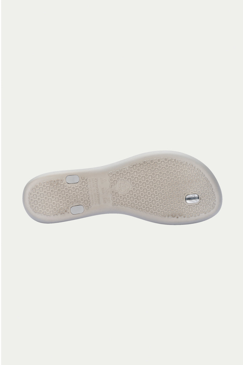 The Ipanema Class Twist Sandal in grey is shown from the bottom, highlighting its textured sole for grip and two small metallic accents embedded in the heel and midfoot areas.