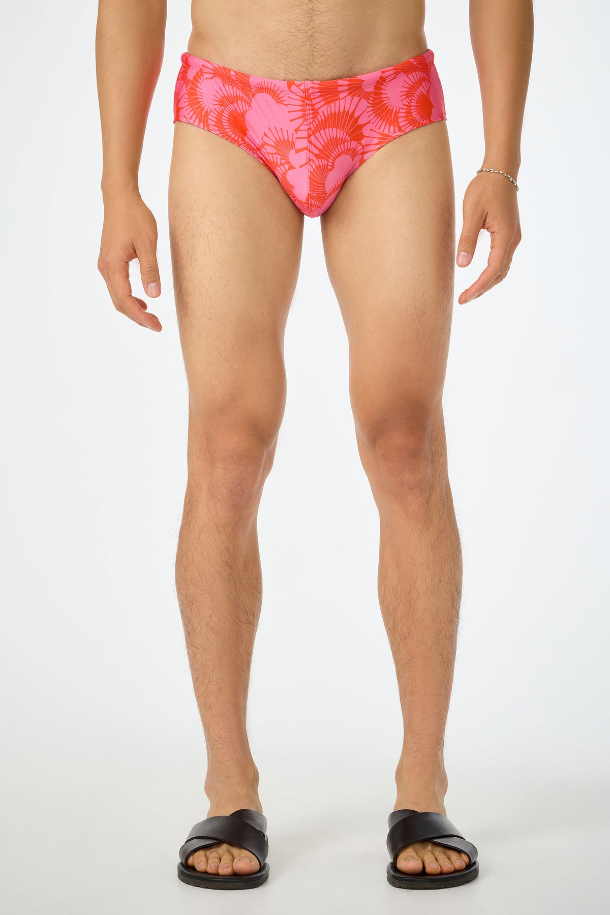 A person stands facing forward, wearing the San Gregorio Swim Brief - Juniper (Multi), black slide sandals, and a silver bracelet. The background is plain white, and the persons head is not visible in the image.