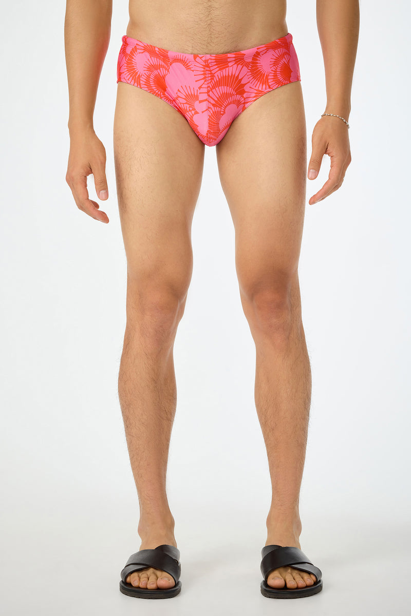 A person stands facing forward, wearing the San Gregorio Swim Brief - Juniper (Multi), black slide sandals, and a silver bracelet. The background is plain white, and the persons head is not visible in the image.