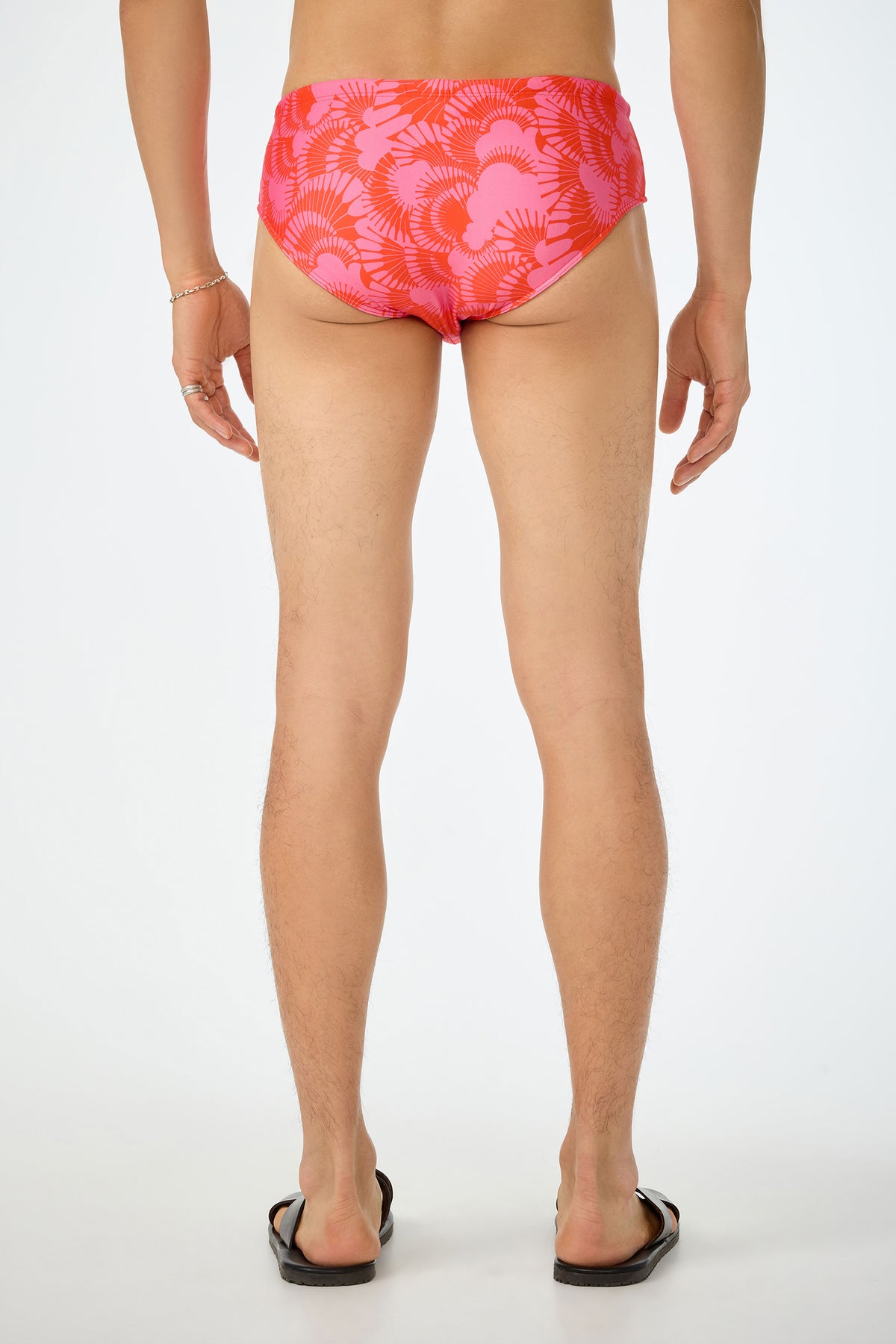 A person with their back to the camera wears the San Gregorio Swim Brief - Juniper and black flip-flops, standing against a plain white background.