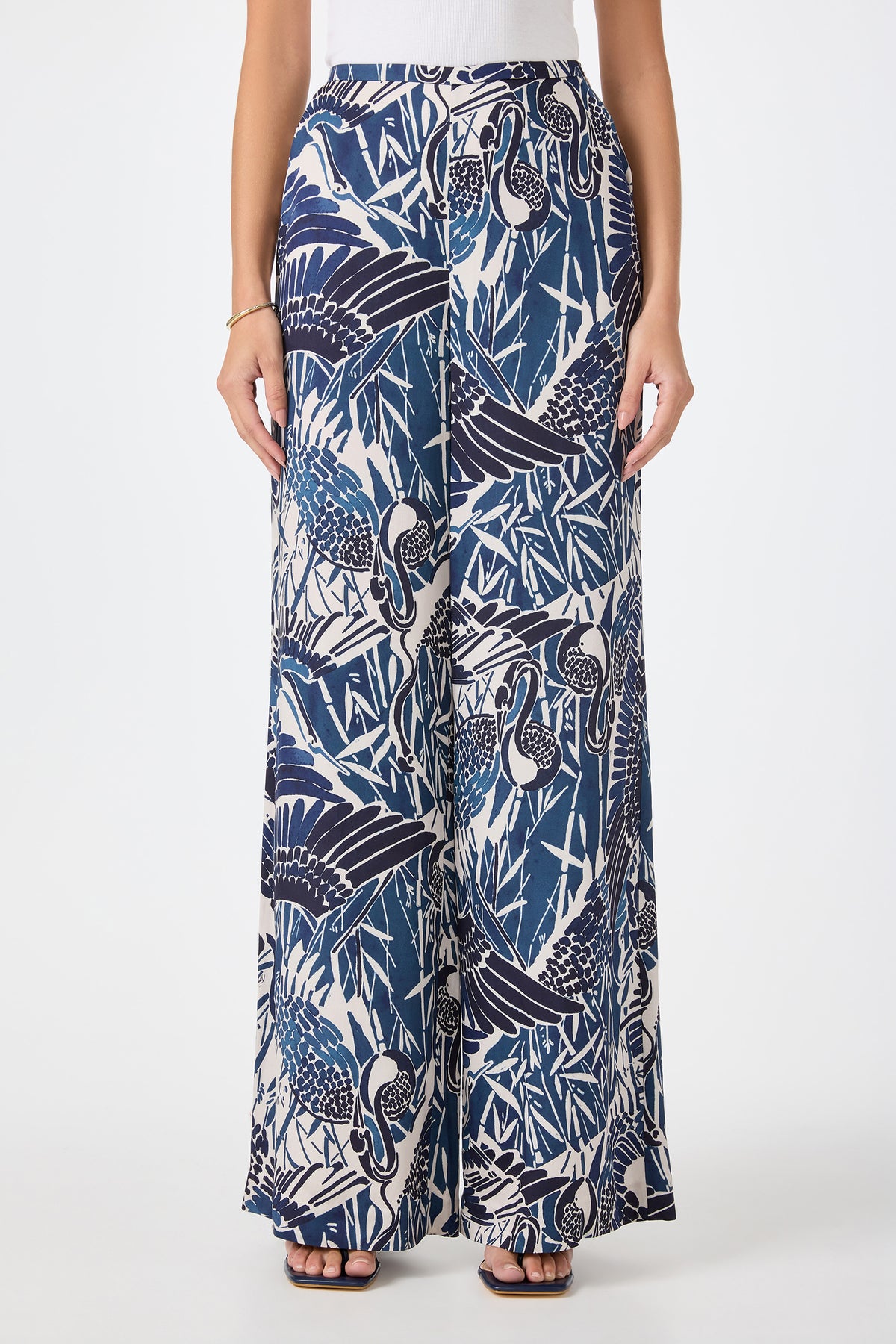 A person wearing the Tavia Wide-Leg Pant in Tsuru—a blue and white tropical crane and foliage print—paired with a white top and black sandals. The image is cropped from shoulders down.