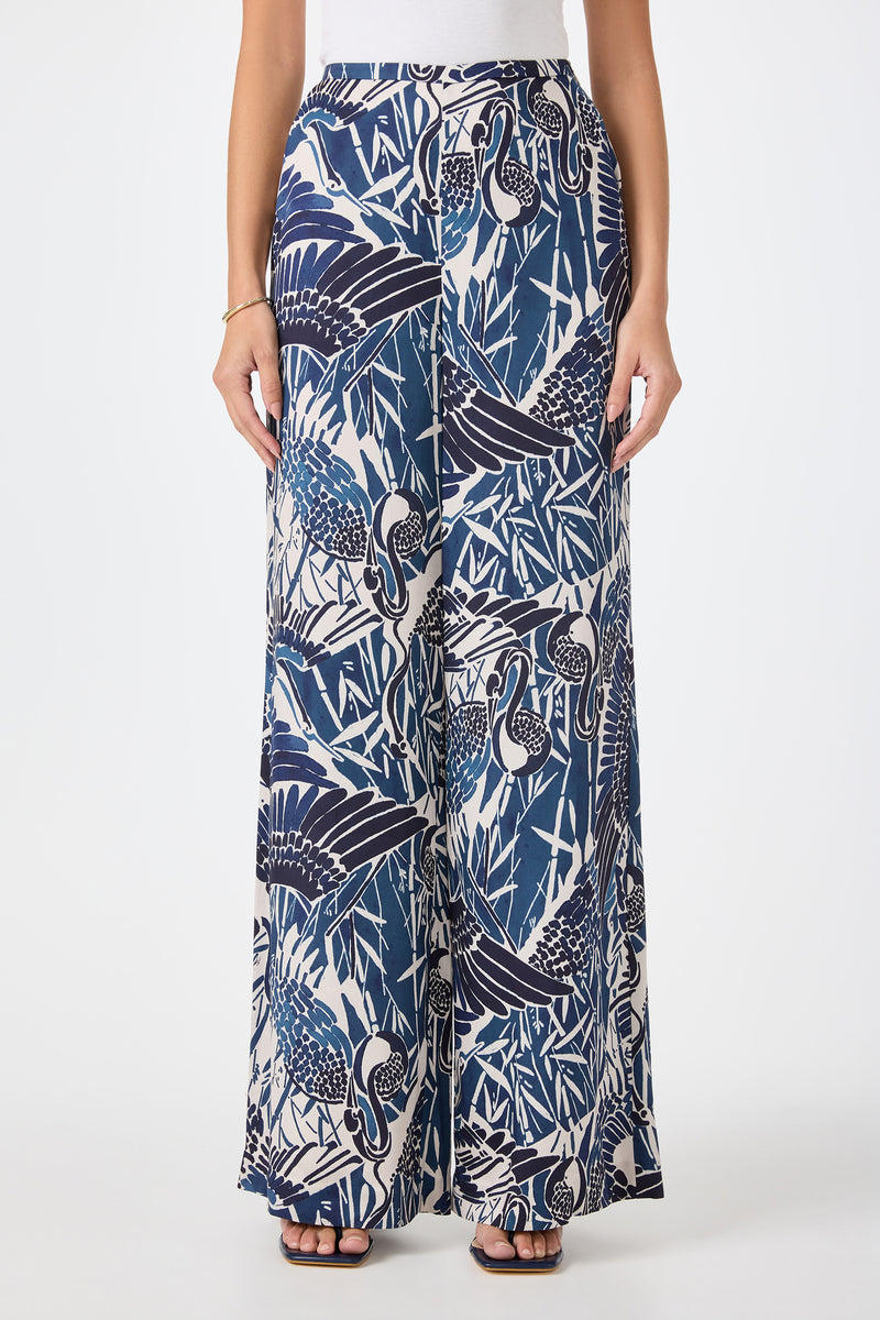 A person wearing the Tavia Wide-Leg Pant in Tsuru—a blue and white tropical crane and foliage print—paired with a white top and black sandals. The image is cropped from shoulders down.