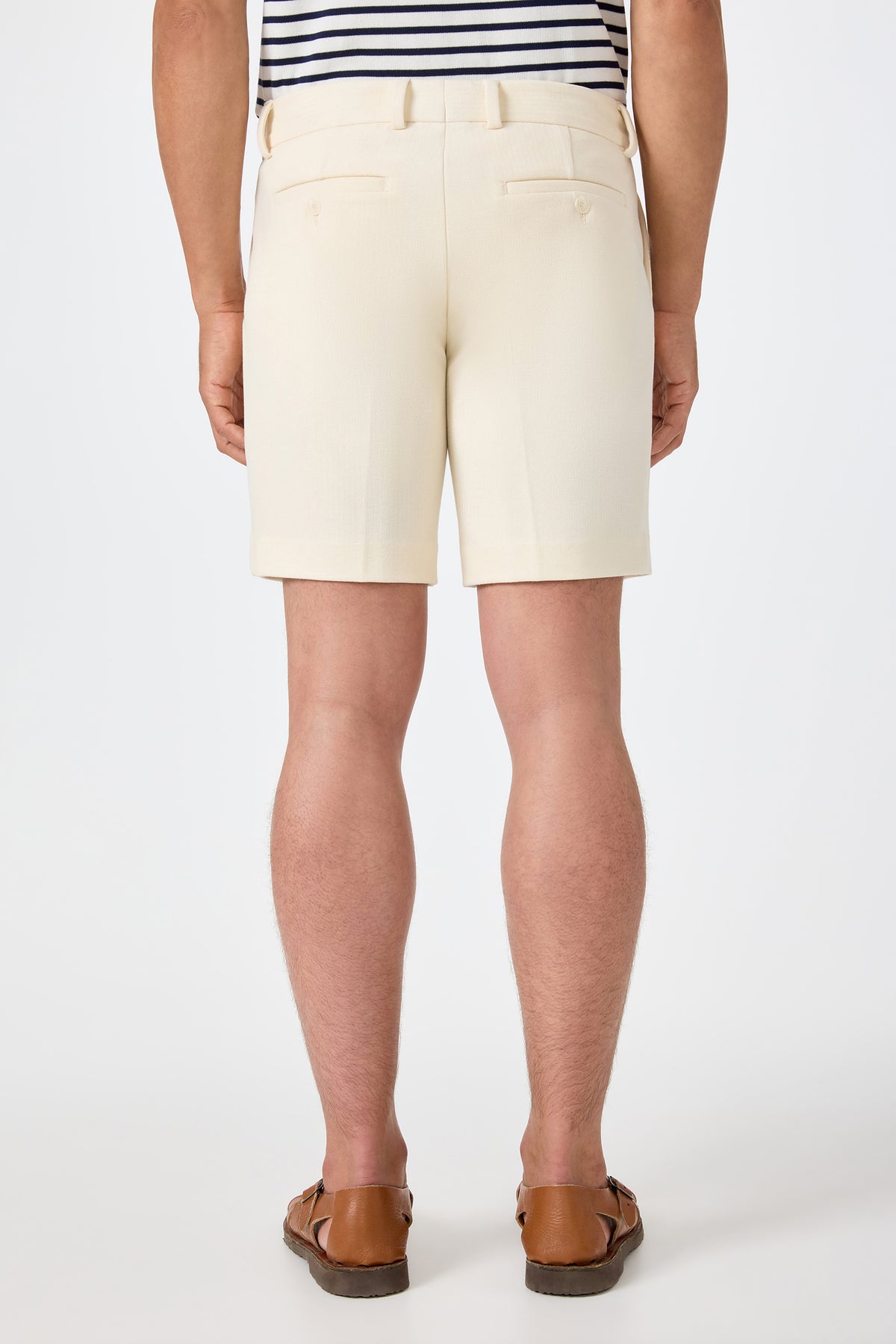 A person stands facing away in the Lawrence Short - Ecru, paired with a striped tucked-in shirt and brown loafers against a plain white background.