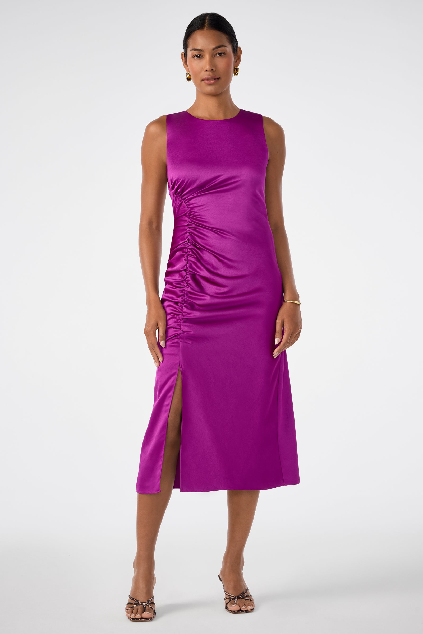 A woman wears the Chestnut Dress, a sleeveless magenta midi with side ruching and a front slit, styled with heeled sandals and minimal jewelry against a plain white background.