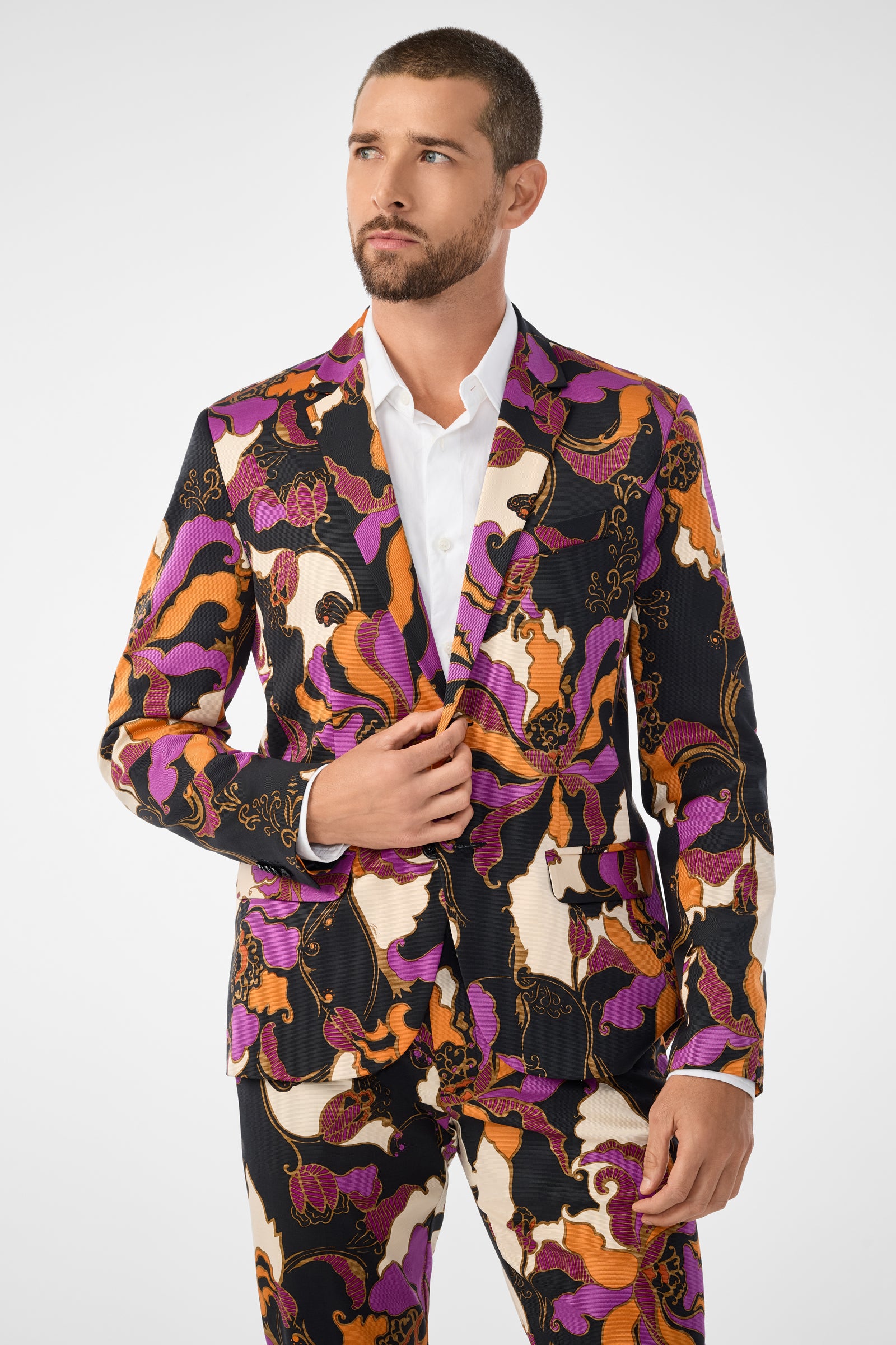 A man wears the Thurston Blazer—a bold, colorful suit with an abstract pattern in purple, orange, black, and cream—over a white shirt, standing against a plain white background.