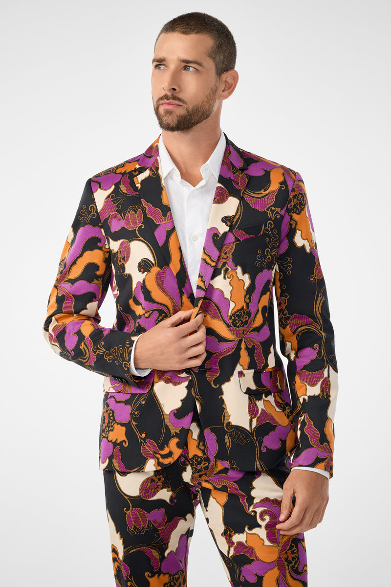 A man wears the Thurston Blazer—a bold, colorful suit with an abstract pattern in purple, orange, black, and cream—over a white shirt, standing against a plain white background.