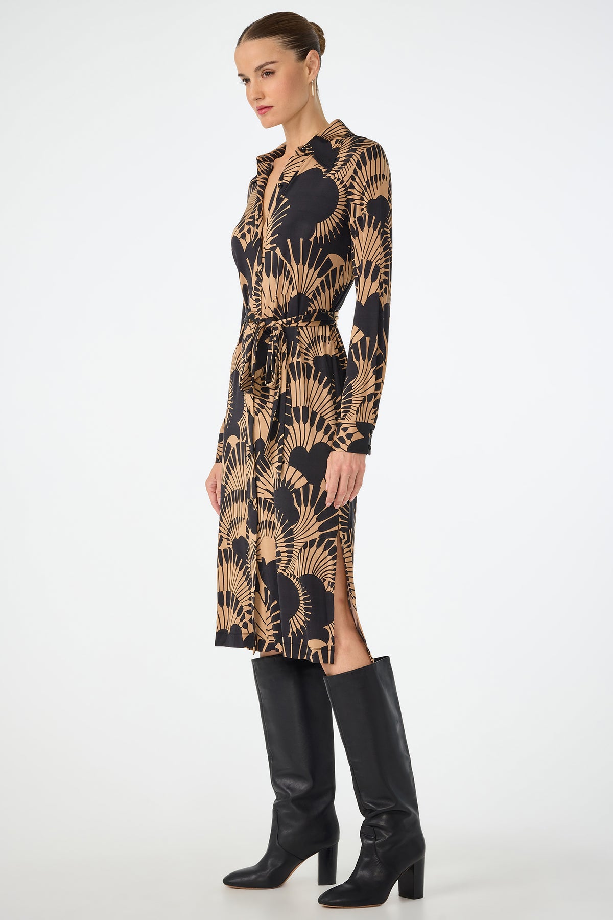 A woman models the Radio City Wrap Dress - Juniper Jersey, a knee-length, long-sleeve dress with a beige and black botanical pattern and waist tie, styled with tall black heeled boots against a plain white background.