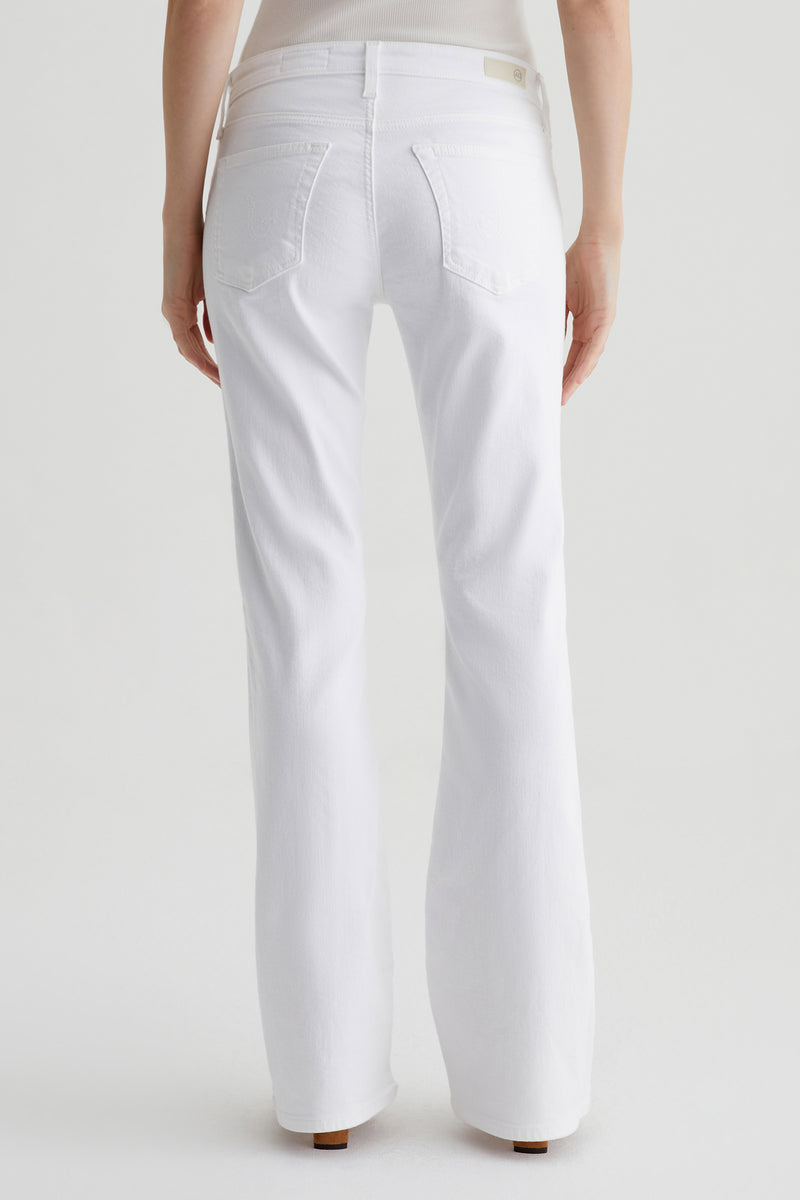 A person stands facing away from the camera, wearing the AG Angel Low-Rise Bootcut Jean in white and a light-colored top, set against a plain white background.
