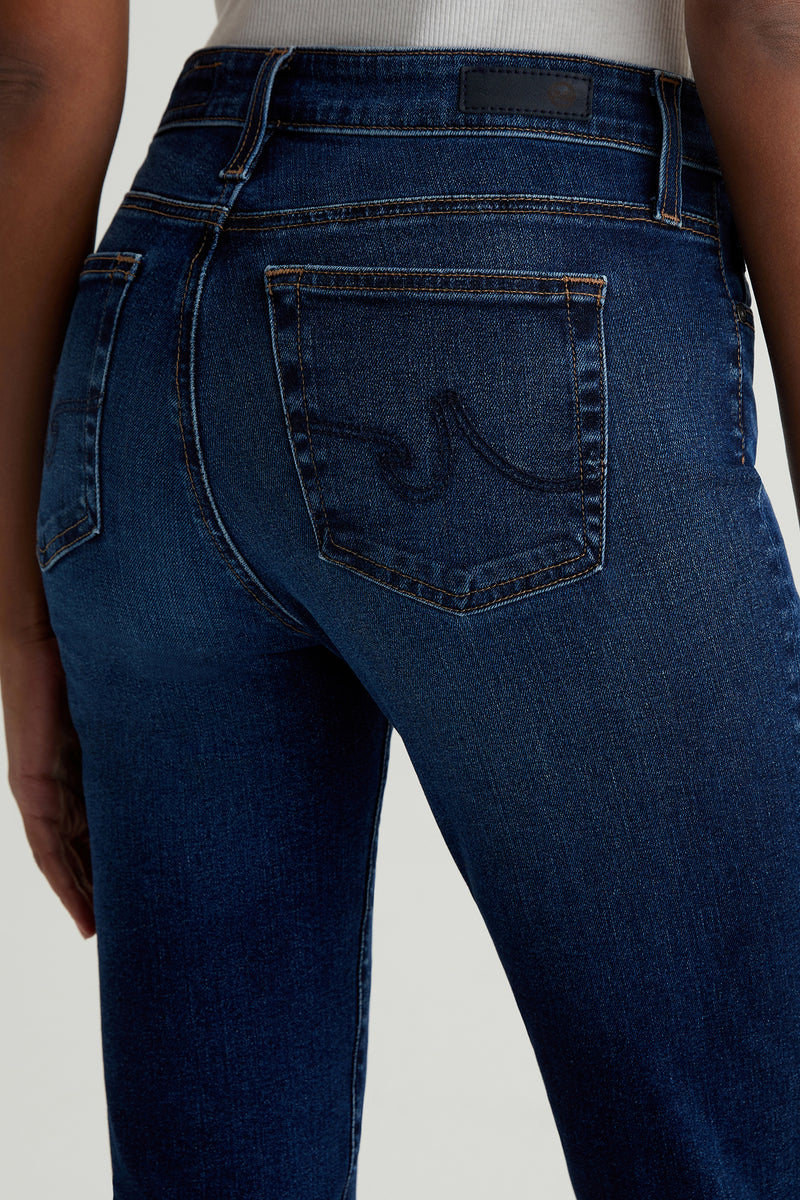 Close-up of a person wearing AG Mari Slim-Straight Crop Jean in Indigo, highlighting the fit, texture, and signature back pocket stitching with part of a white top tucked in.