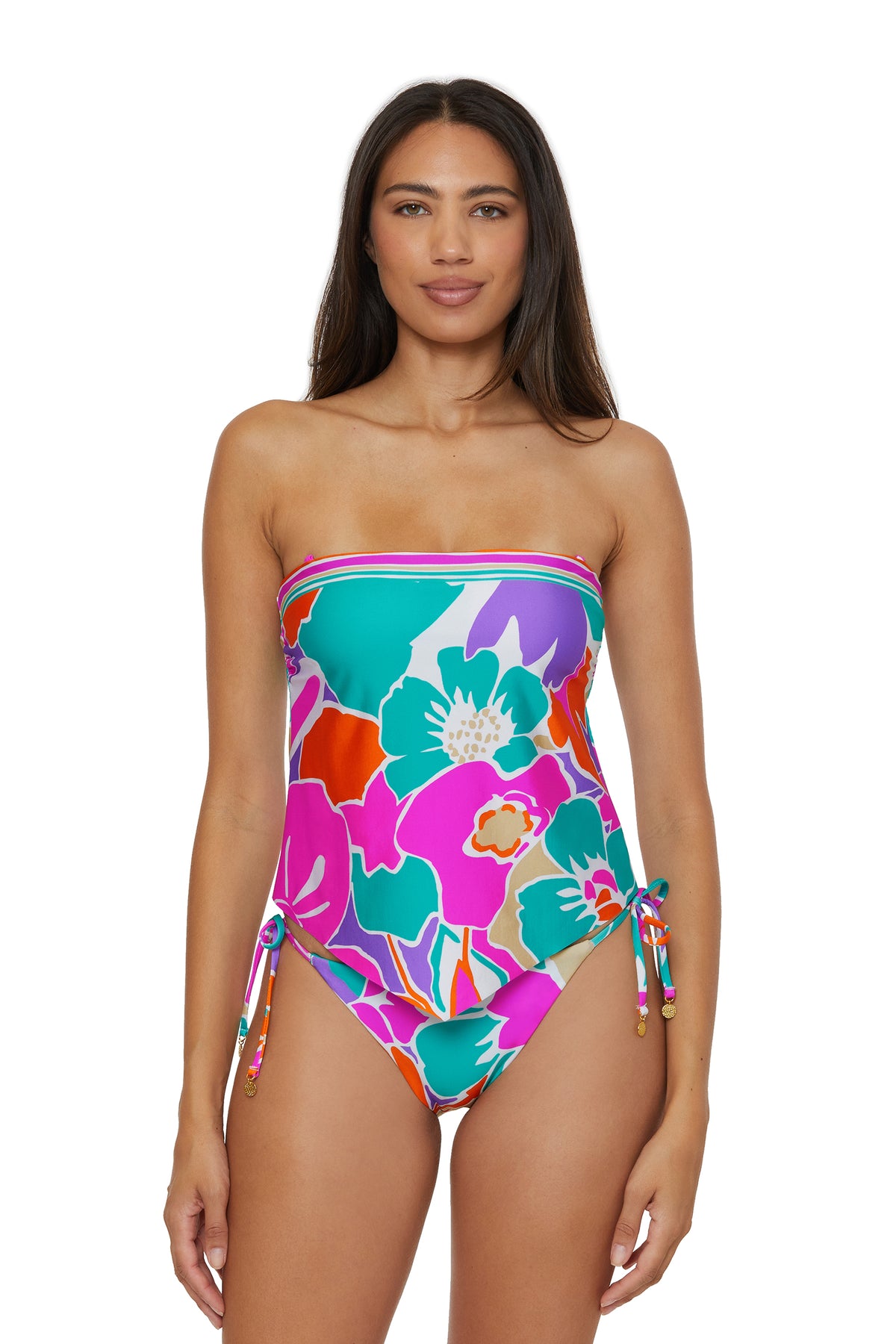A woman with long brown hair wears the TRINA TURK SWIM Handkerchief Tankini Swim Top - Amalfi, featuring a bold floral pattern in pink, teal, green, and orange. She stands against a white background.