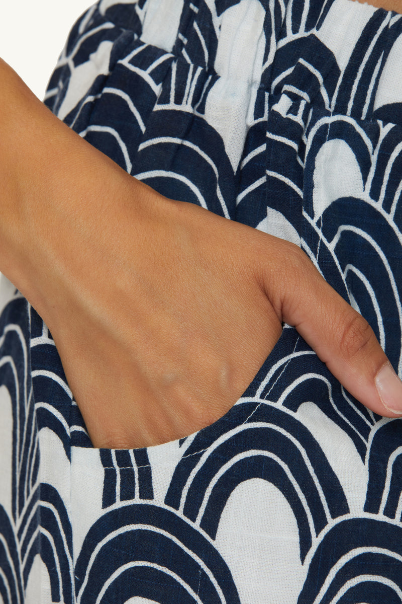 A close-up of a hand resting in the pocket of the Swim Cover-Up Short - Arches, featuring white fabric with a navy blue curved geometric design.