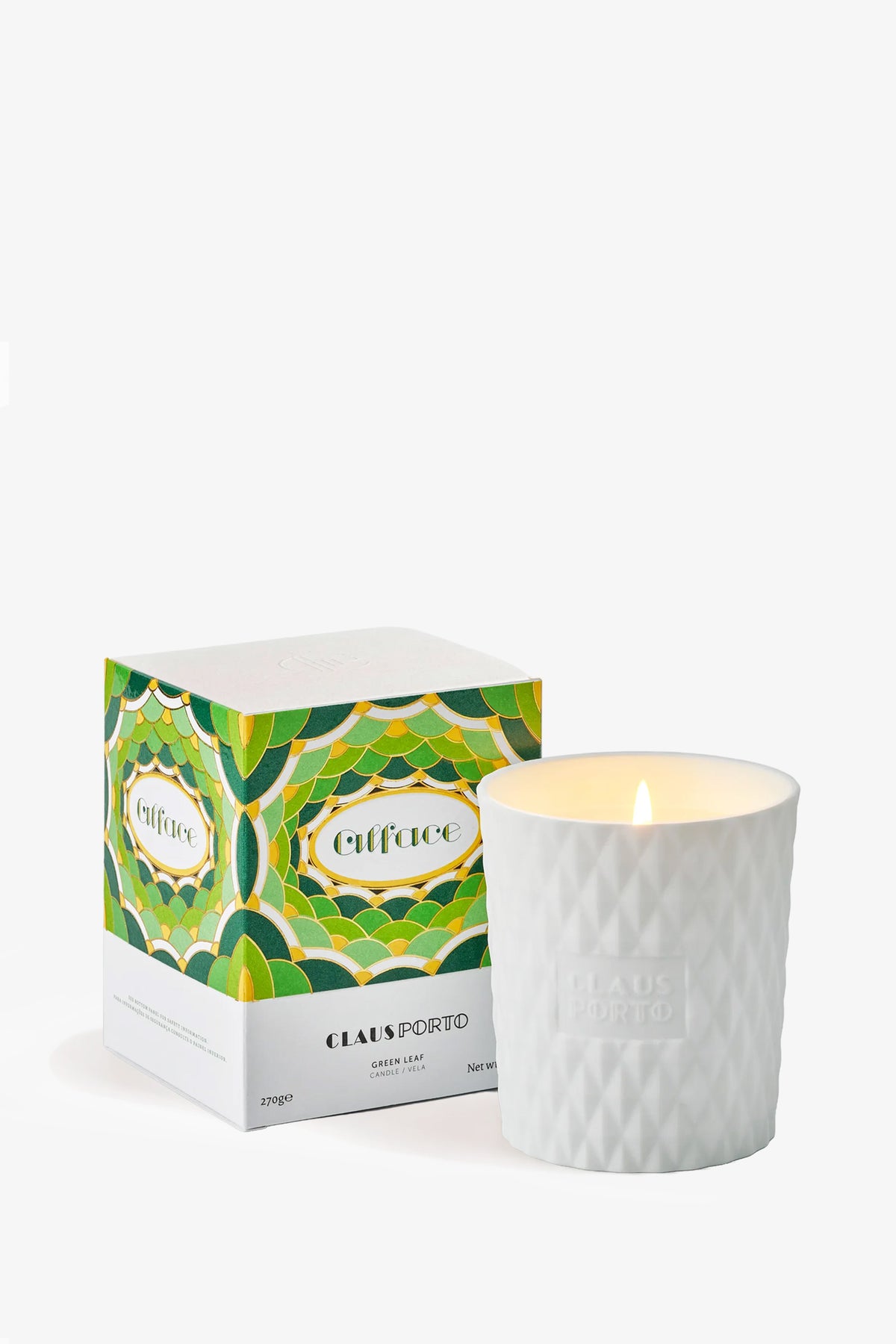 A lit Claus Porto Alface Candle in a textured glass holder sits beside its colorful, green-patterned box.