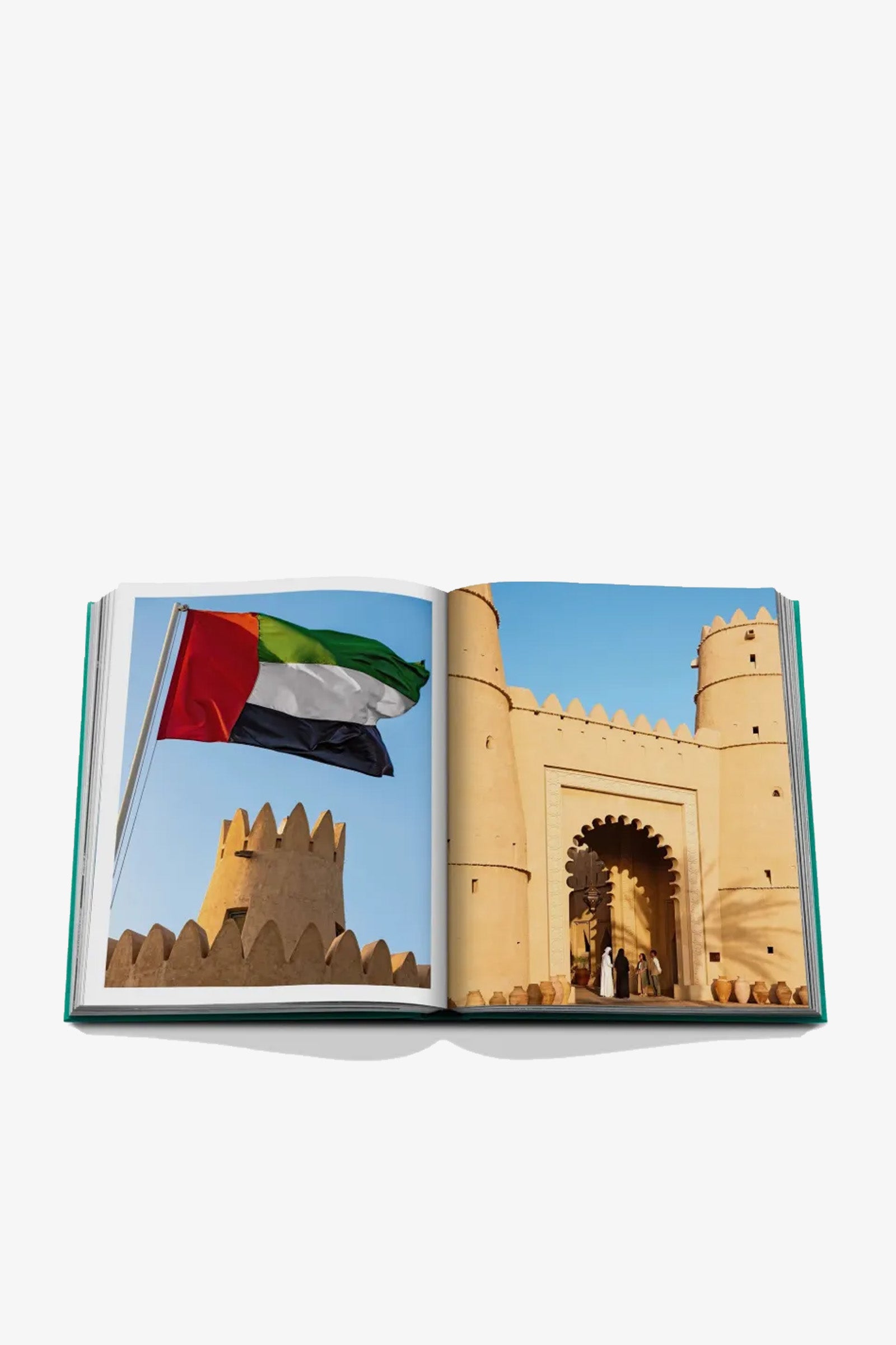 An open Assouline Abu Dhabi Book displays a photo of the UAE flag and a second image of a historic beige fort with an arched entrance set against a clear blue sky.
