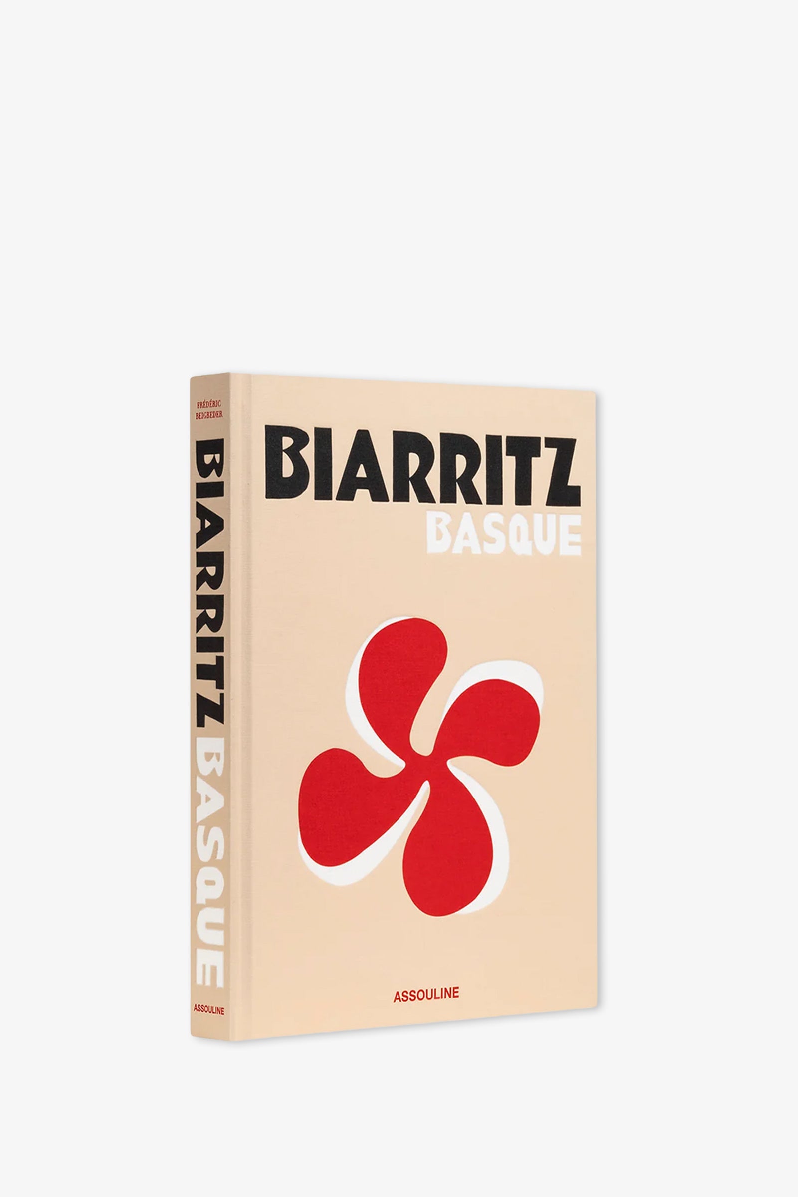 The Assouline Biarritz Basque Book is a beige hardcover featuring a striking red Basque cross symbol on its cover. The book’s spine displays the title, while the publisher, ASSOULINE, is printed at the bottom.