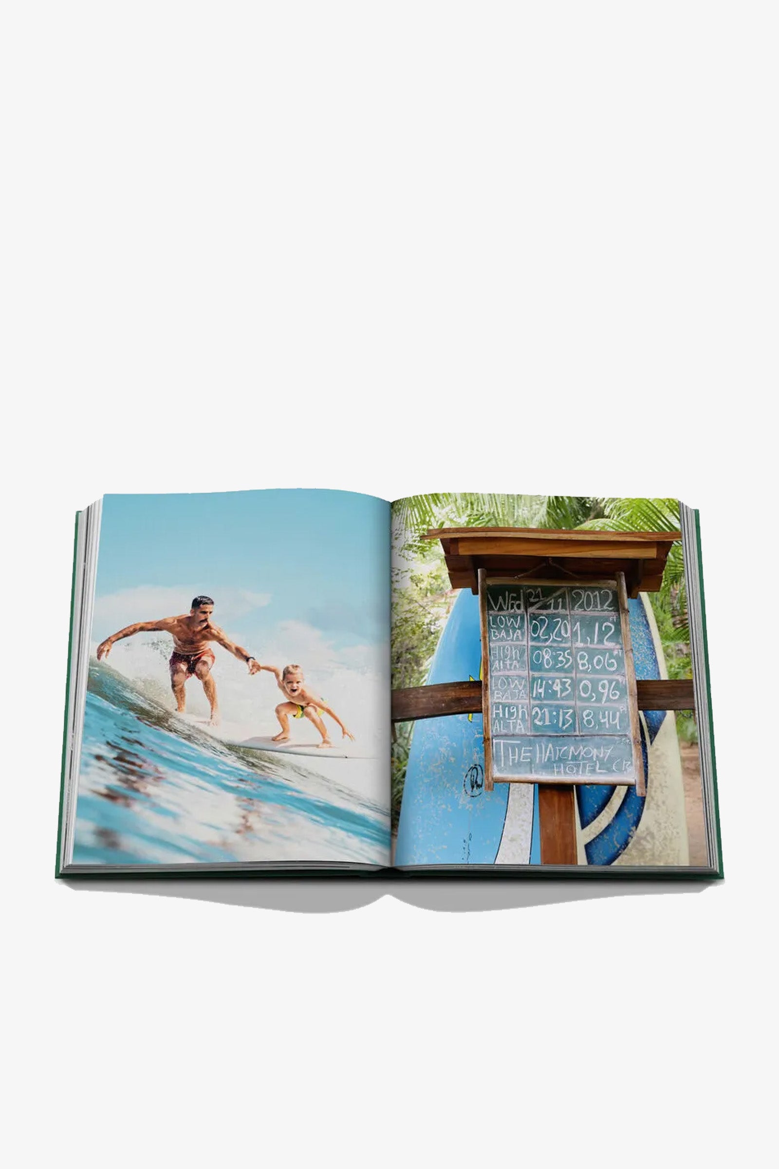 An open Assouline Costa Rica Vida Book displays a surfing duo riding a wave on the left page, while the right page features a surfboard sign with dates and numbers next to blue surfboards.