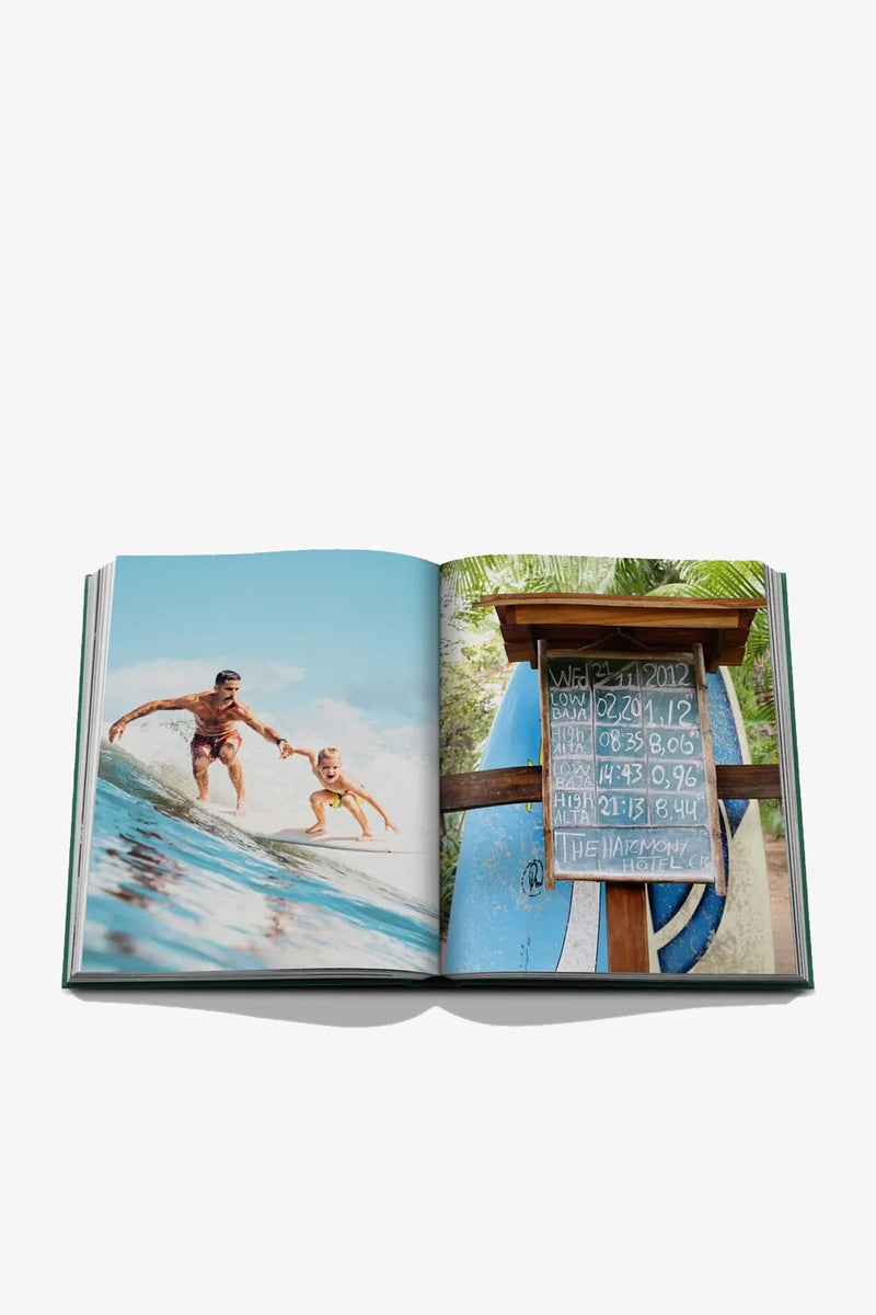 An open Assouline Costa Rica Vida Book displays a surfing duo riding a wave on the left page, while the right page features a surfboard sign with dates and numbers next to blue surfboards.