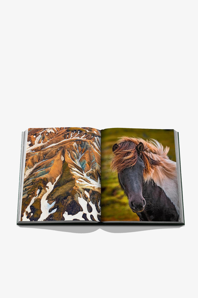 The Assouline Iceland Epic Book is open, revealing a landscape with snow and brown terrain on the left page and, on the right page, a close-up image of a black horse with a windswept mane.