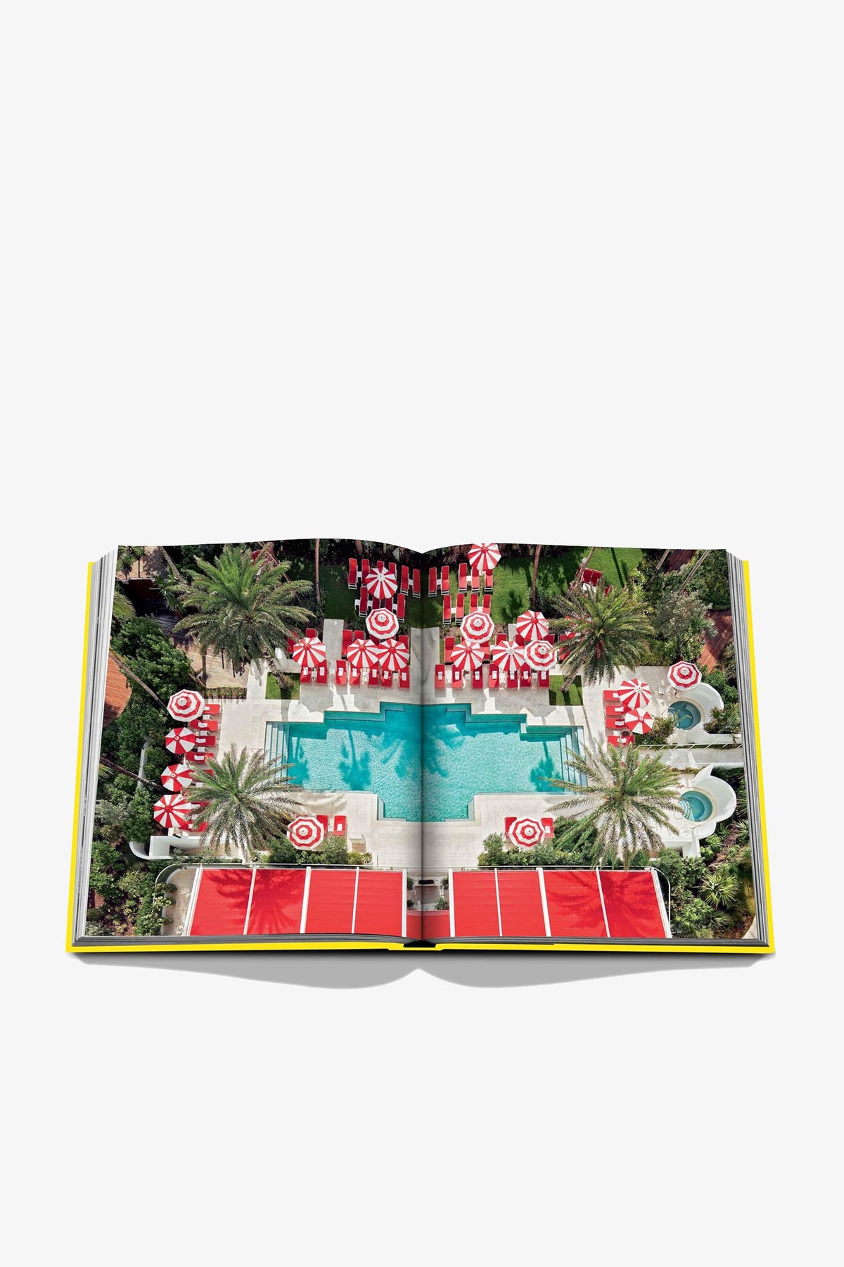 An open Assouline Miami Beach Book displays an aerial photo of a pool surrounded by palm trees, red-and-white umbrellas, sun loungers, and a vibrant outdoor setting.