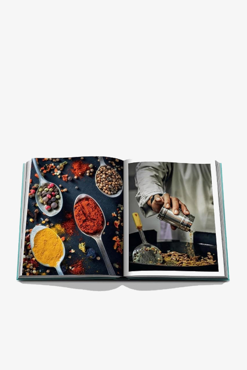 An open copy of the Assouline Saudi Arabia: Red Sea Book displays vivid images, with one page featuring colorful spices arranged on spoons and the opposite page showing a person sprinkling spices into a pan.