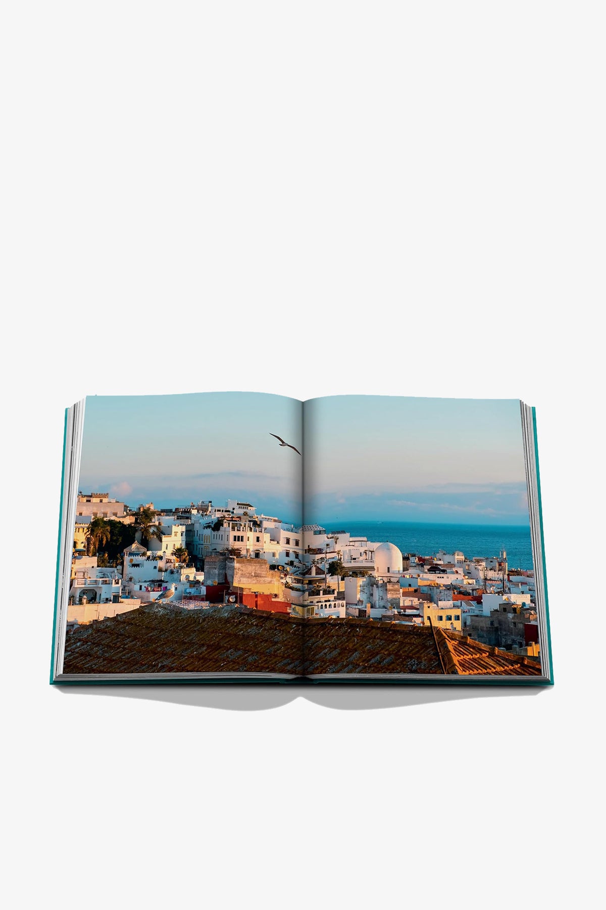 An open Assouline Tangier Tangerine coffee table book featuring a panoramic photograph of a dense hillside city overlooking the sea.