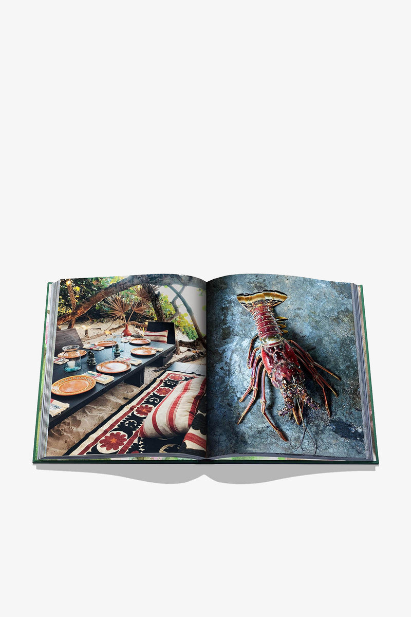 An open Assouline Tulum Gypset Book displays a coastal dining scene on the left page and a spiny lobster on a textured surface on the right page.