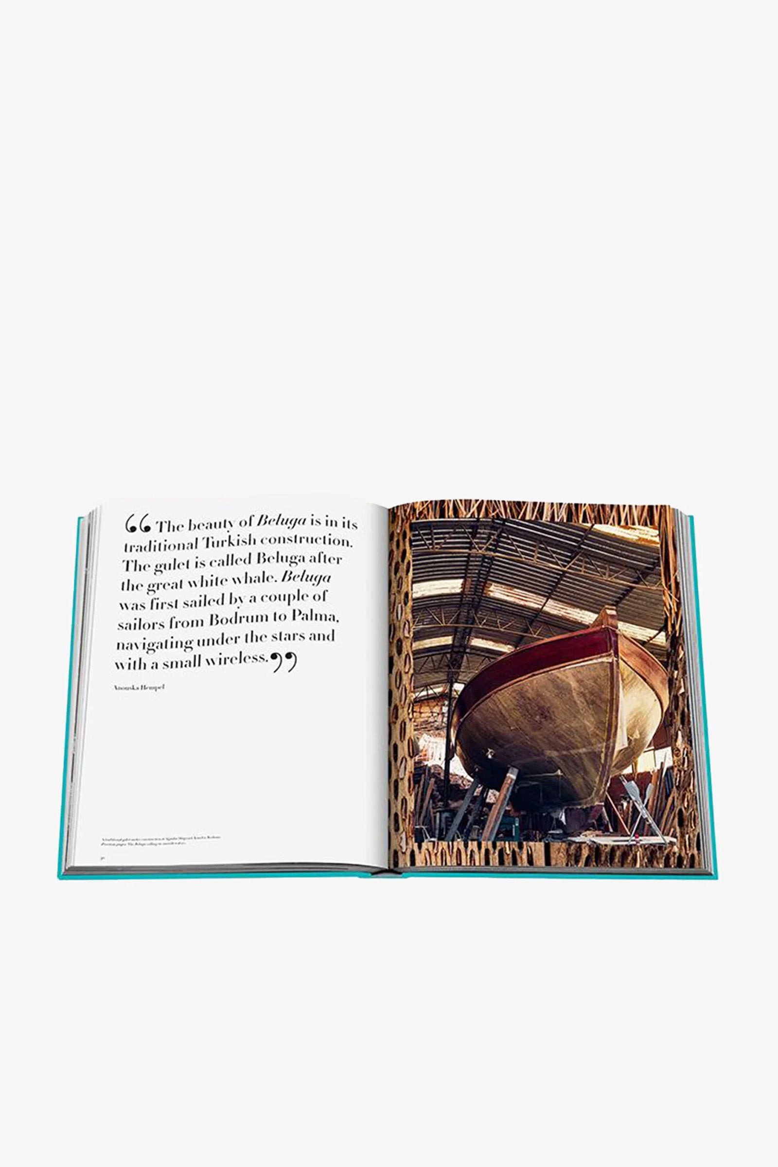 An open Assouline Turquoise Coast Book displays a quote about a traditional Turkish boat on the left page and a photo of a large wooden boat in a workshop on the right page.