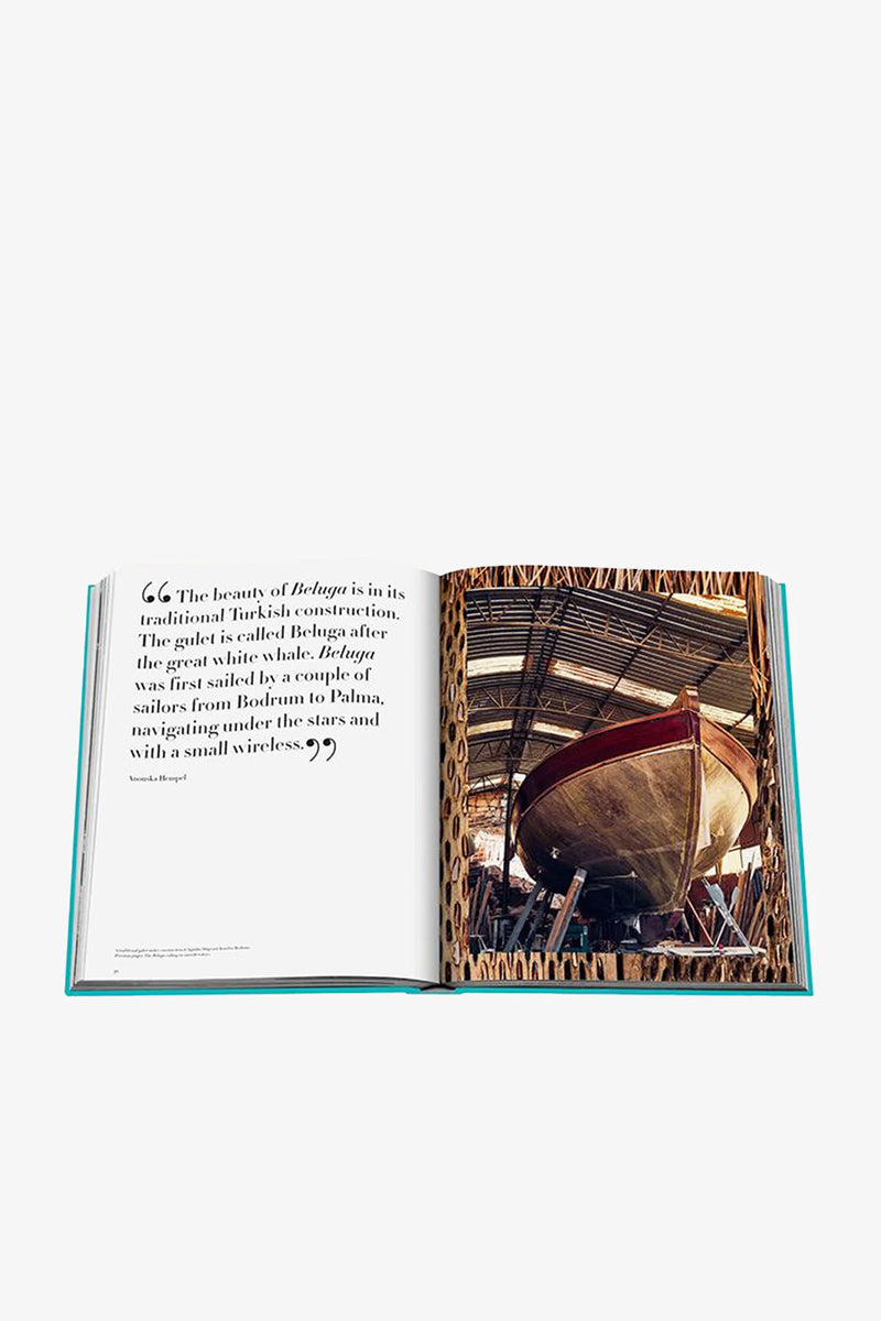 An open Assouline Turquoise Coast Book displays a quote about a traditional Turkish boat on the left page and a photo of a large wooden boat in a workshop on the right page.