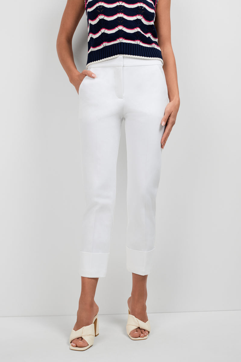 A person stands against a plain white background wearing Banshee Cropped Cuff Hem Pants, a sleeveless knit top with wavy stripes, and cream open-toe heeled sandals. Their hands are in their pockets.