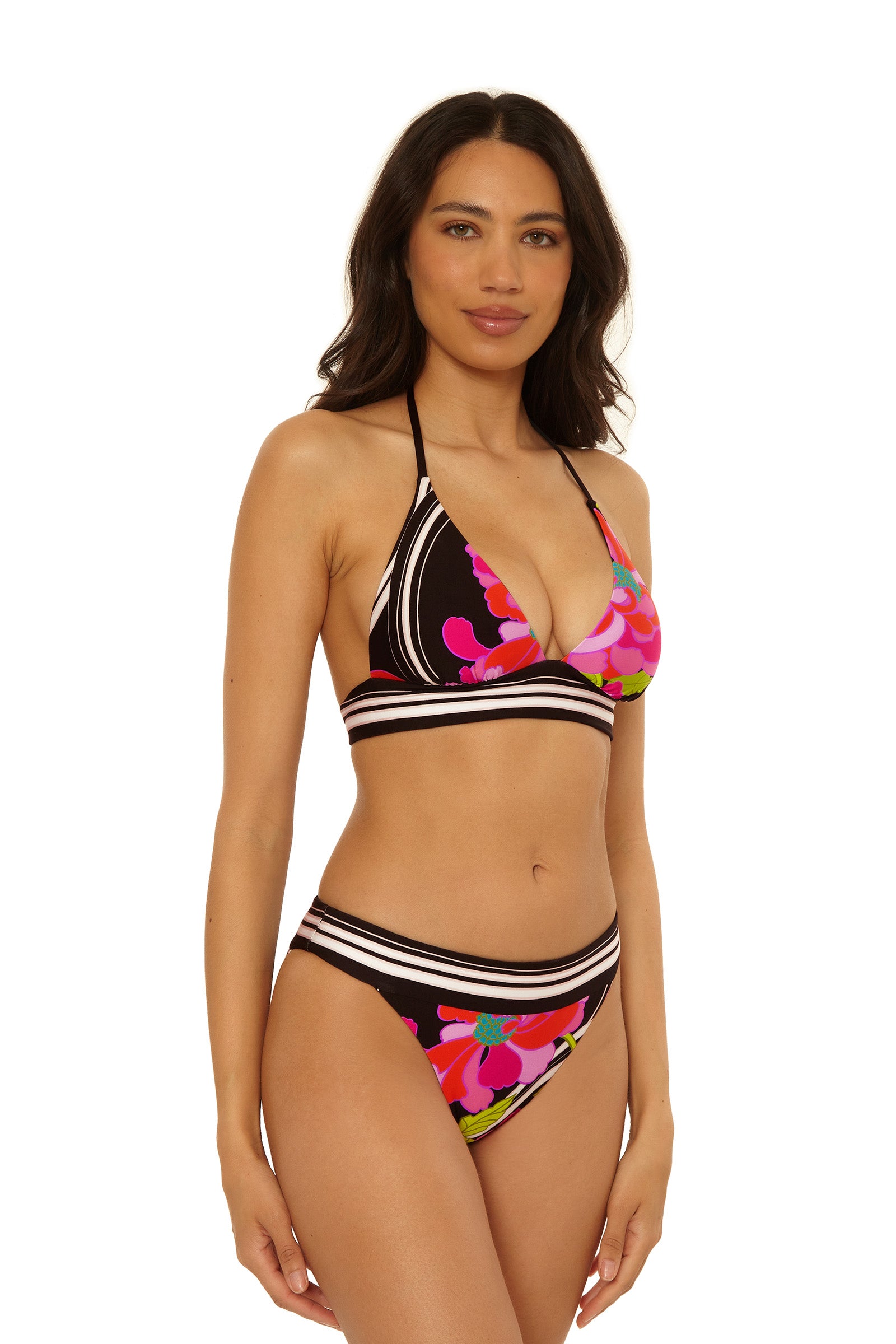 A woman with long, wavy dark hair wears the Reversible Halter Swim Top - Bougainvillea, featuring a bold geometric and floral pattern in black, white, pink, red, green, and blue. The bikini has a halter top and mid-rise bottom.