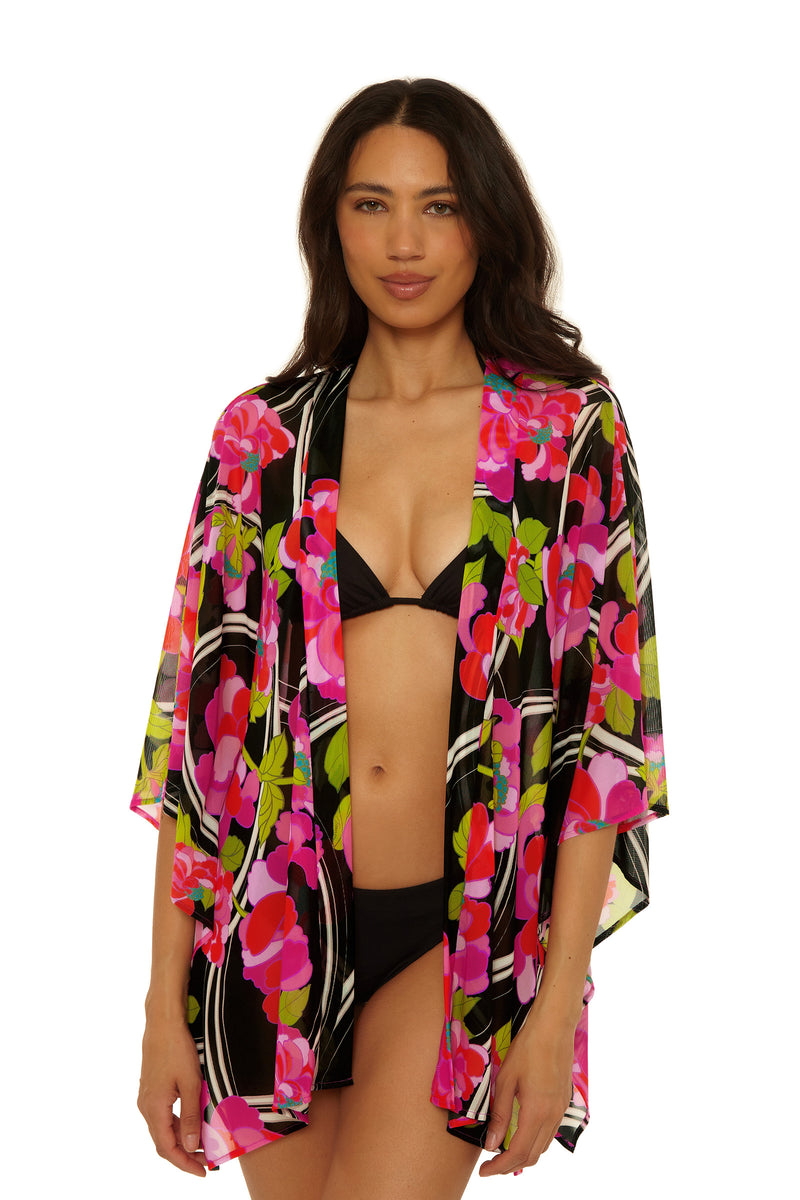 Woman models the Kimono Swim Cover-Up - Bougainvillea in Bougainvillea Swim Knit, featuring vibrant floral patterns over a black bikini, standing against a white background with a relaxed expression.