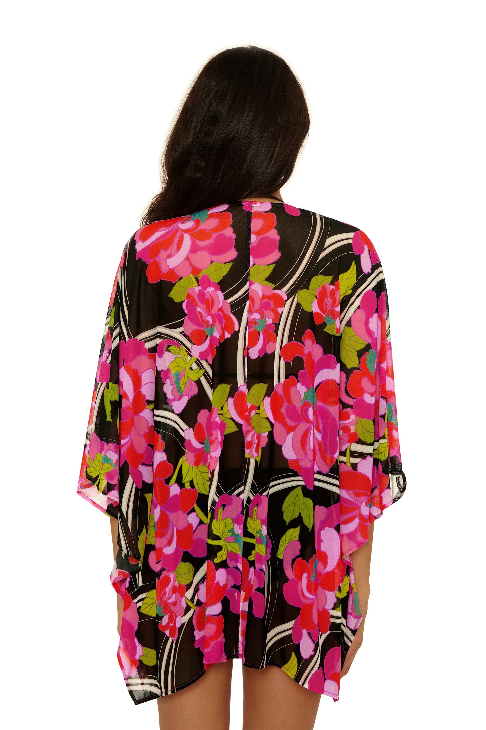 A woman with long dark hair is seen from behind, wearing the Kimono Swim Cover-Up - Bougainvillea, featuring bright pink, red, and green floral patterns on a black background. Her arms rest naturally by her sides.