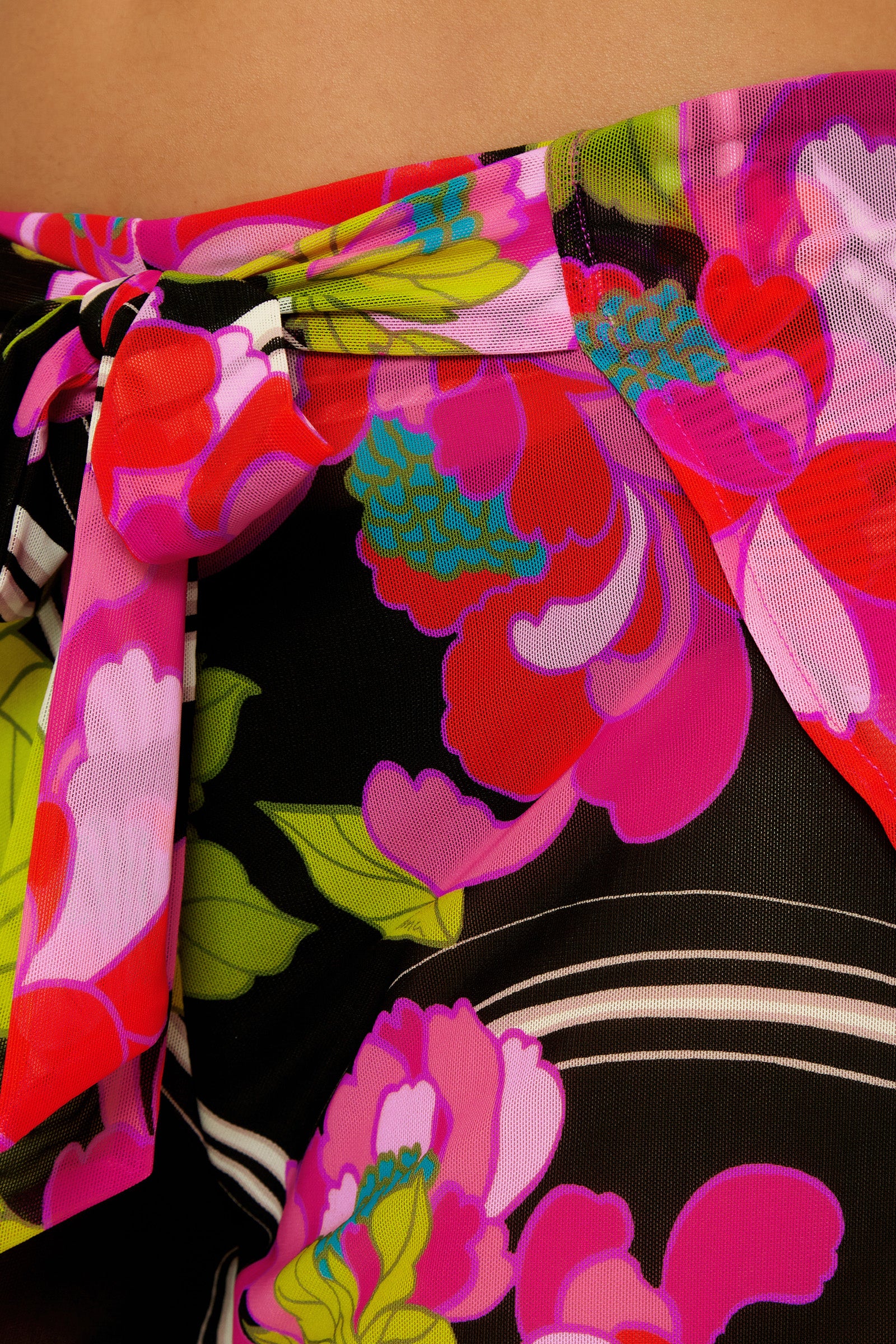 A close-up of the Wrap Cover-Up Short - Bougainvillea, showcasing its vibrant pink, red, green, and blue floral pattern on a black background with a decorative side knot.