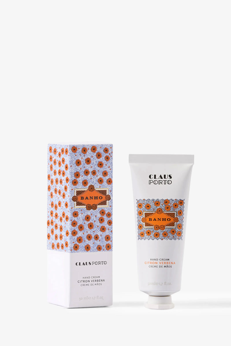 A tube and box of Claus Porto Banho Hand Cream, featuring a vibrant orange and blue geometric design. The upright tube is positioned beside its coordinating box against a plain white background.