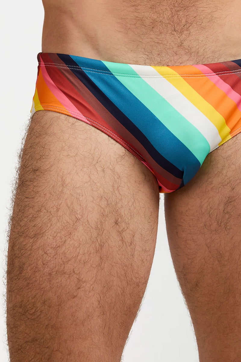 A close-up of a person wearing the Bondi Swim Brief - Siena Stripe, highlighting the colorful striped swimsuit and the wearer’s upper thighs.