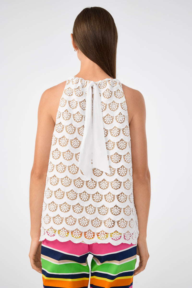 A woman seen from behind wears the Rancho Crochet Halter Top, a sleeveless white lace top with a scalloped pattern and neck bow, paired with colorful striped pants in pink, orange, green, blue, and black.