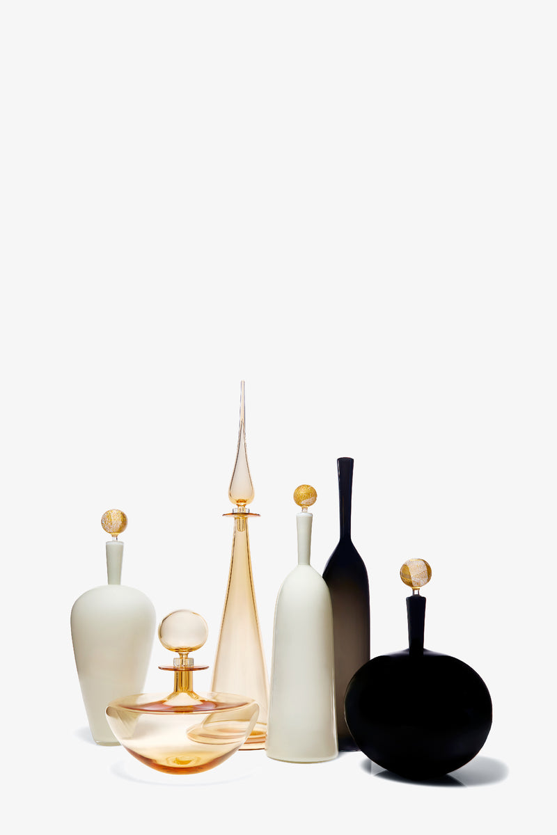 The Carmella Barware Low Round set features six elegant glass and ceramic bottles in assorted shapes and sizes with round gold stoppers, displayed together on a white background.