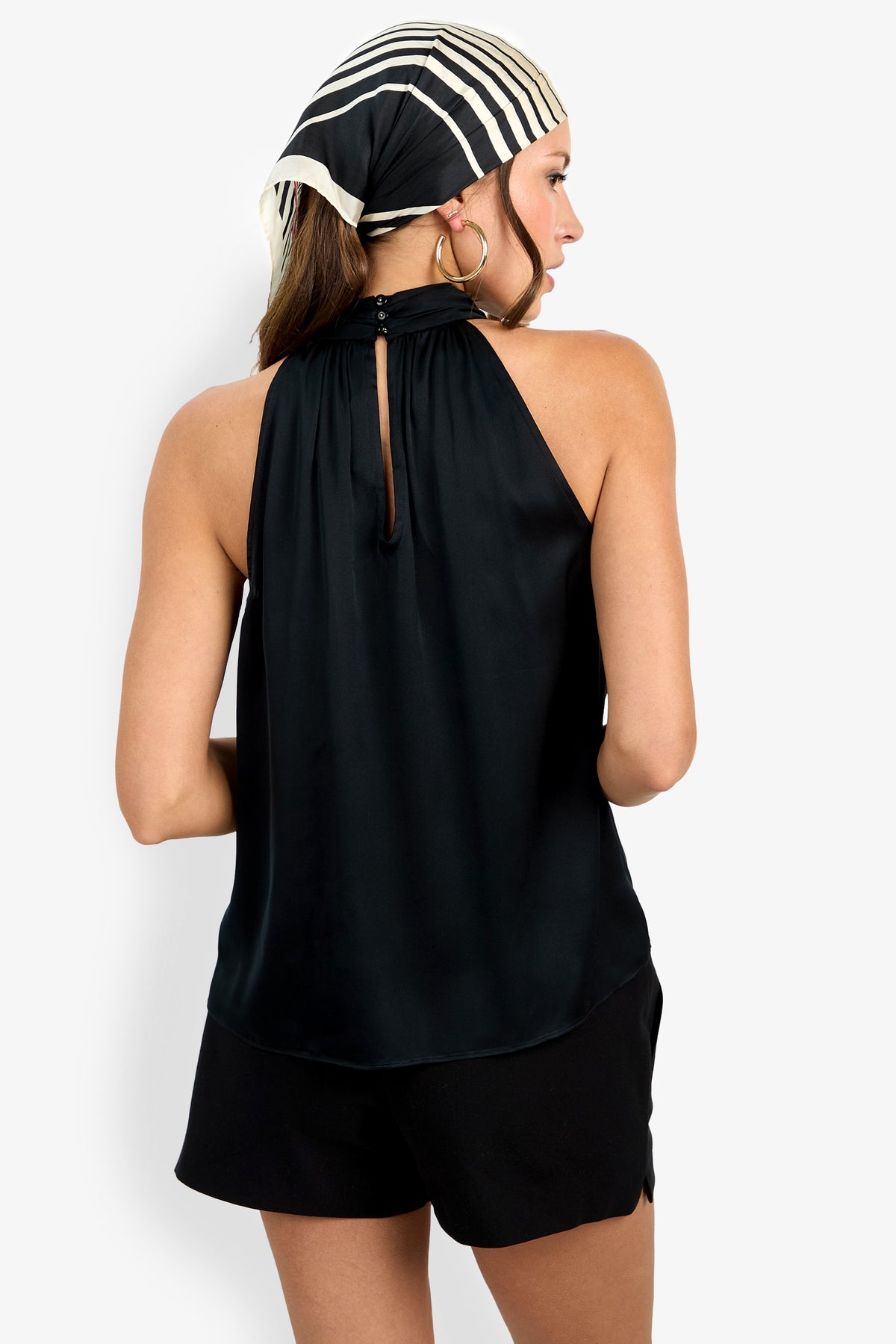 A woman with long hair wears the Zana Top in black and is facing away from the camera, highlighting its back keyhole detail.