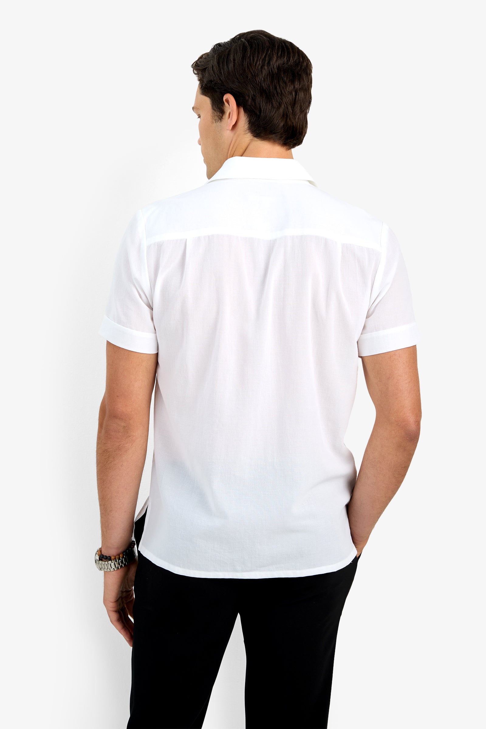 A man with short brown hair stands with his back to the camera, wearing the Will Shirt (short-sleeved, white) and black pants, set against a plain white background.