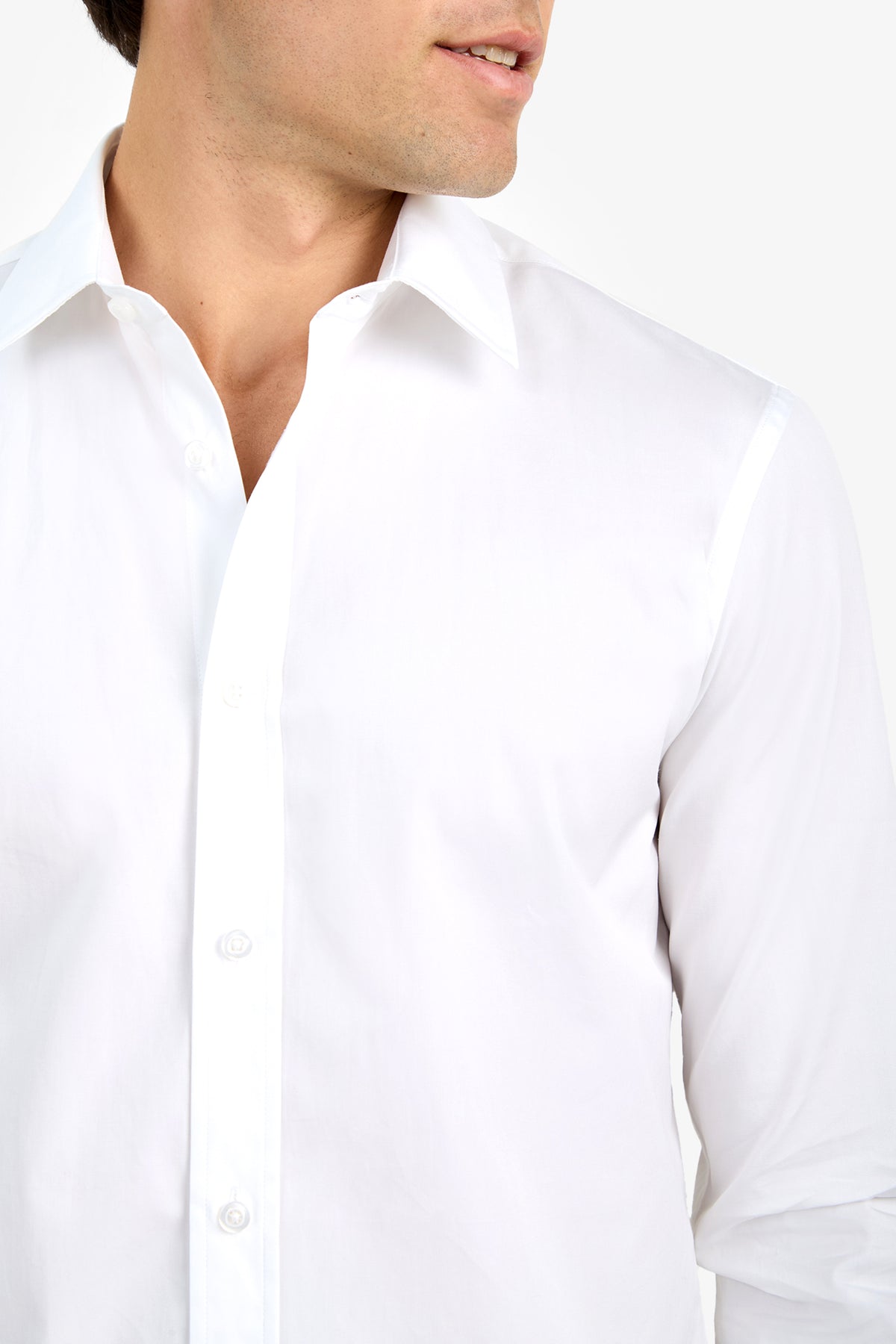 A man models the Aaron Shirt—a crisp white button-up—photographed from shoulders to mid-torso, head partially visible and turned slightly to the side against a plain white background.