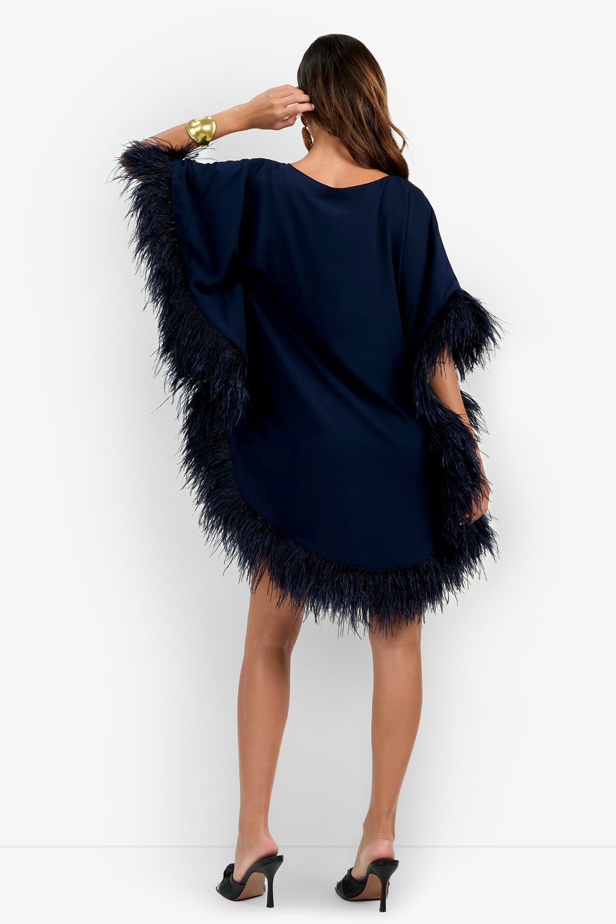 Woman wearing the Mini Neena Fringe Dress in navy blue, styled with black heels, posing with her back to the camera and her hand touching her hair.